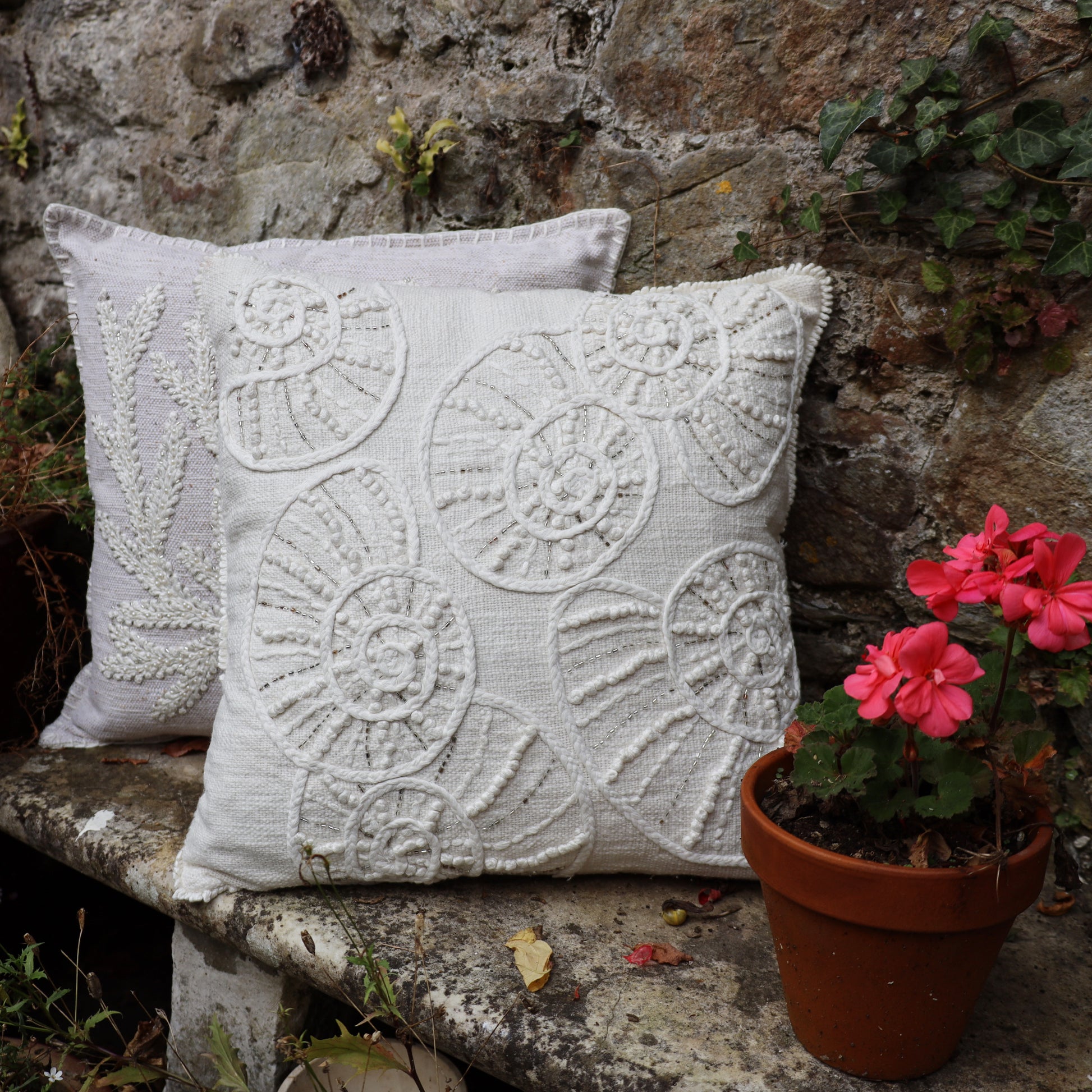 Decorative pillows with floral patterns on a stone bench next to a potted plant.