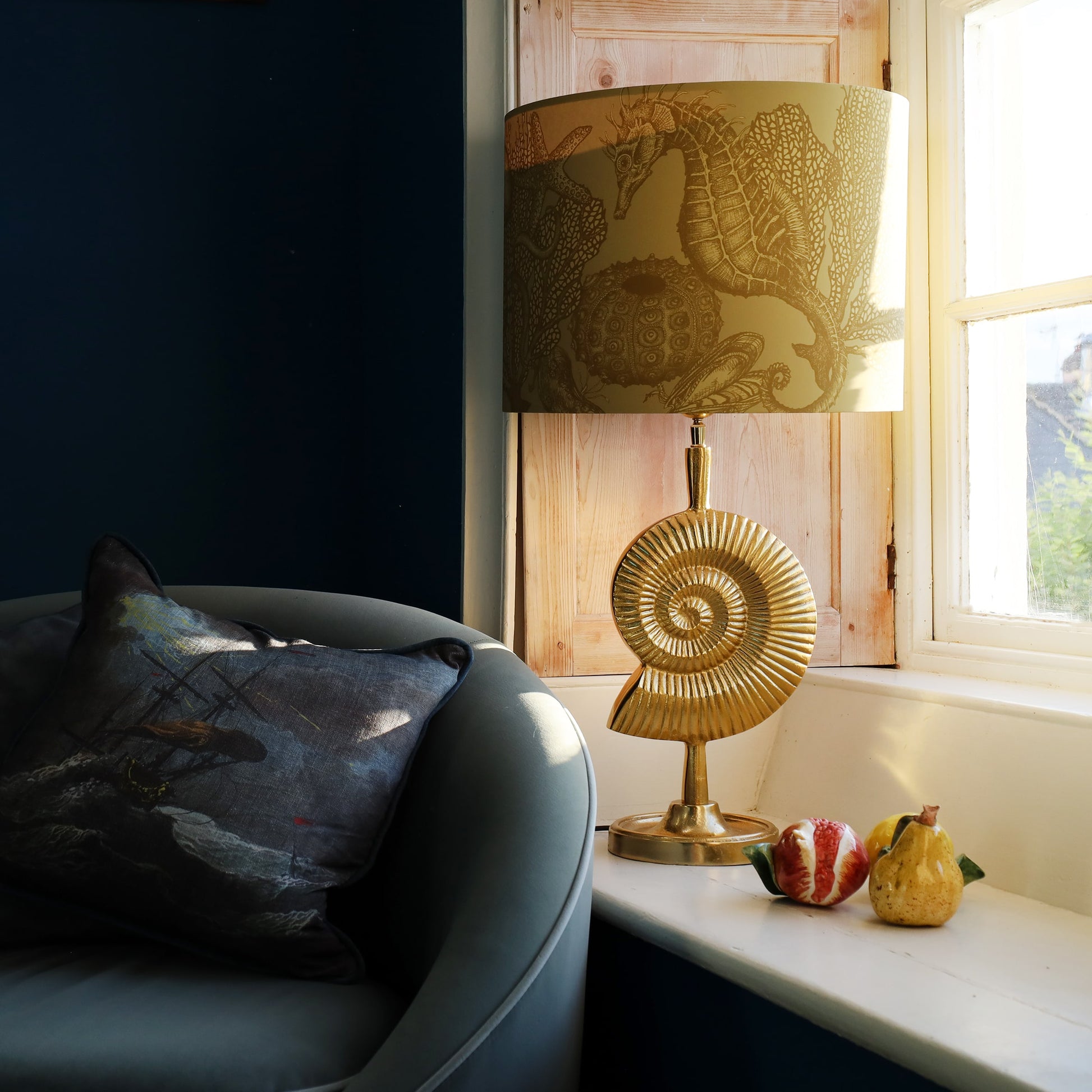 Gold ammonite lamp with decorative shade on a windowsill next to a gray sofa.
