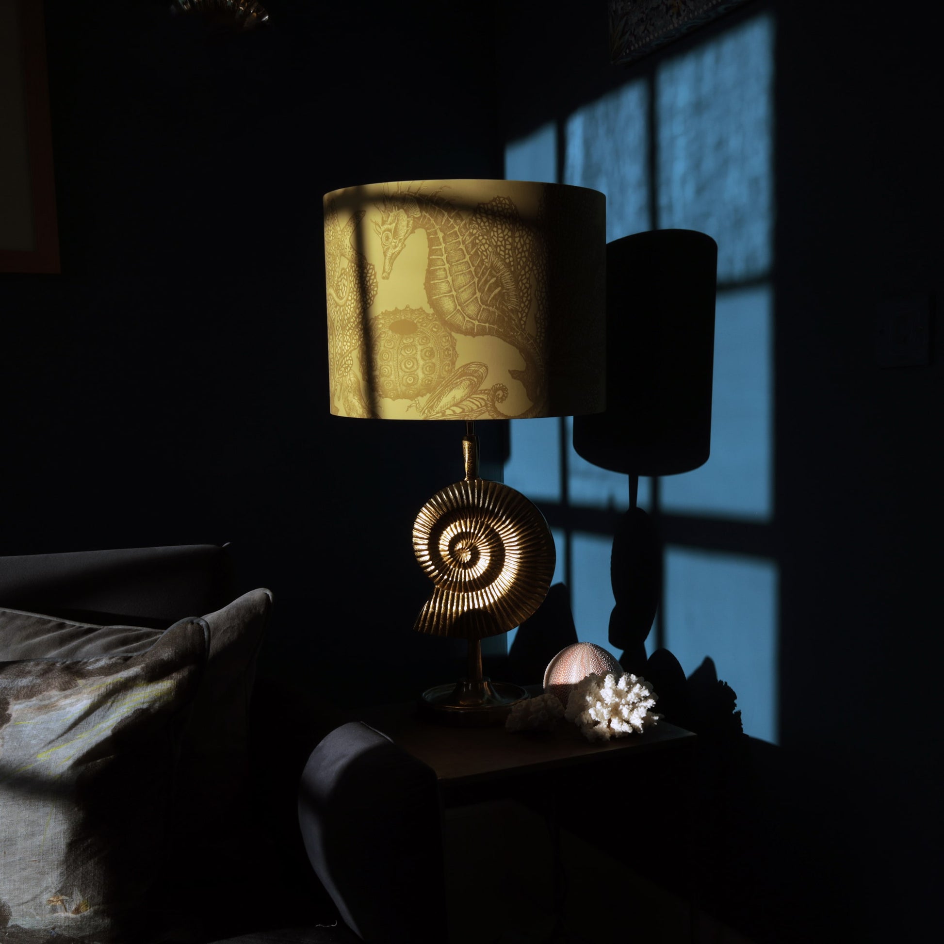 Decorative gold ammonite lamp with a patterned shade on a dark surface