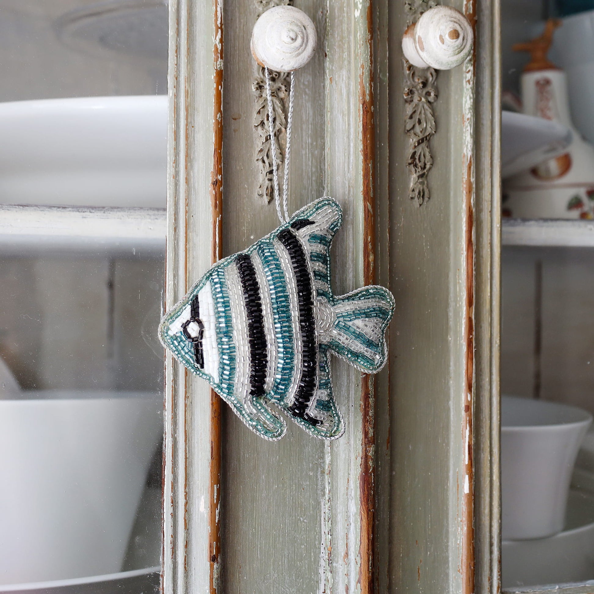 Decorative fish ornament hanging on a decorative mirror with a blurred kitchen background.