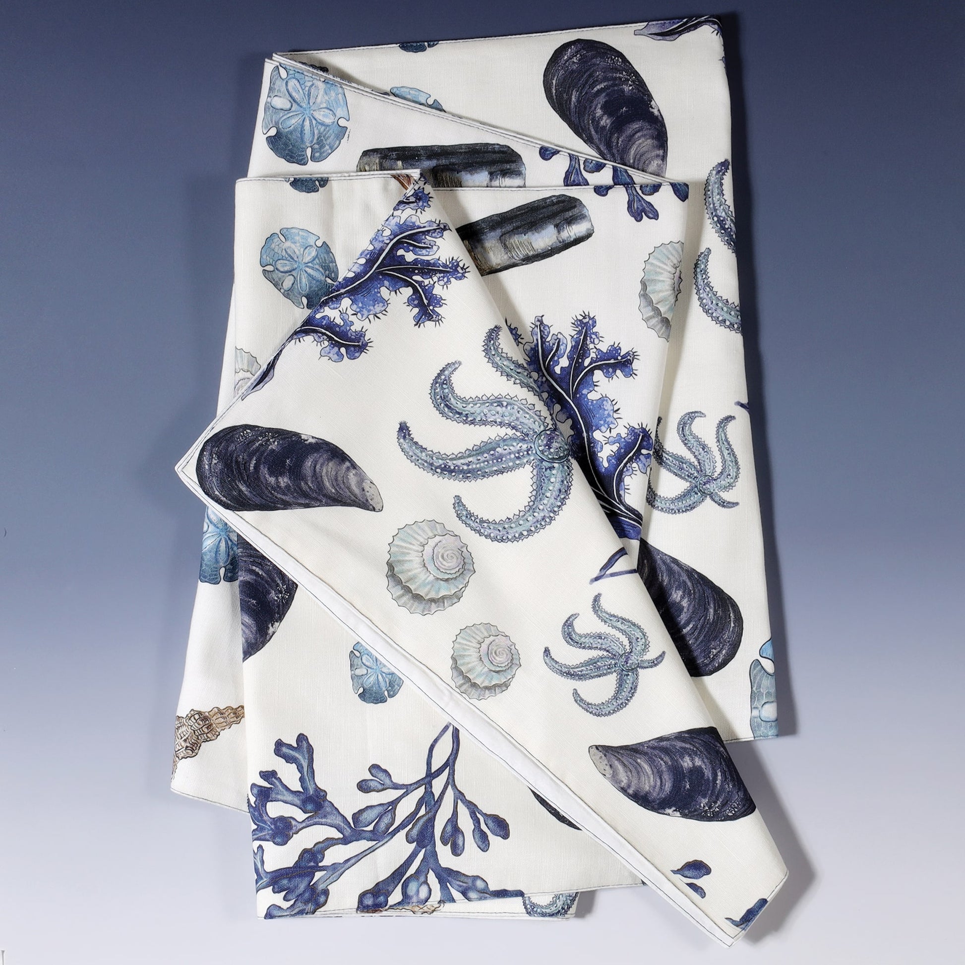 Cotton and Linen mix table runner with hand drawn illustrations with our Rockpool design of Sea life and Shells in shades of Blue folded to show different shells