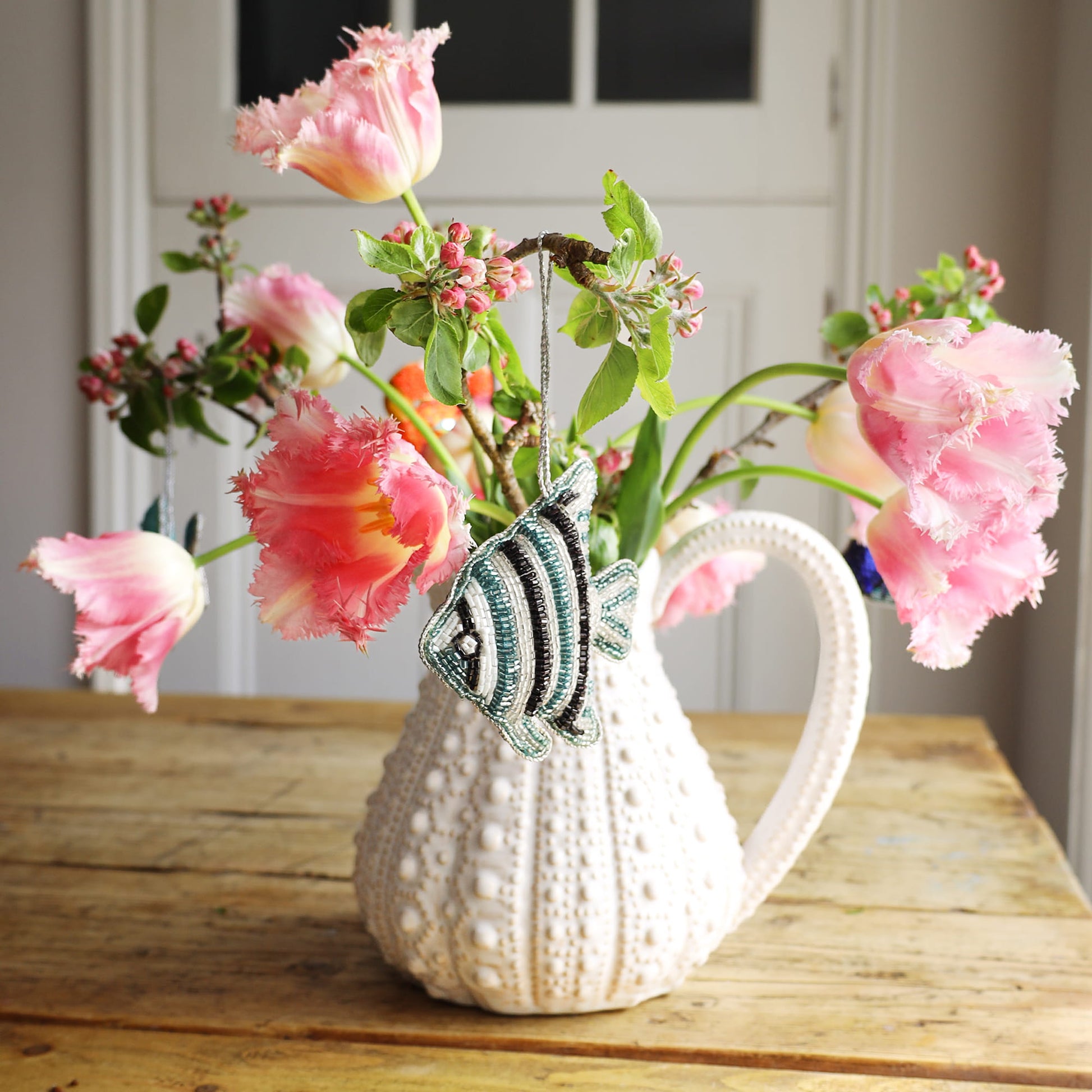 Decorative urchin jug with pink flowers and a fish ornament on a wooden surface.
