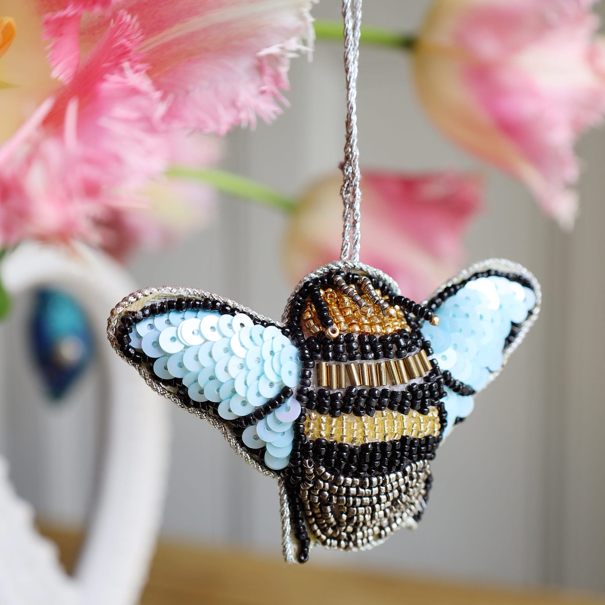 Decorative bee ornament with sequins against a blurred floral background