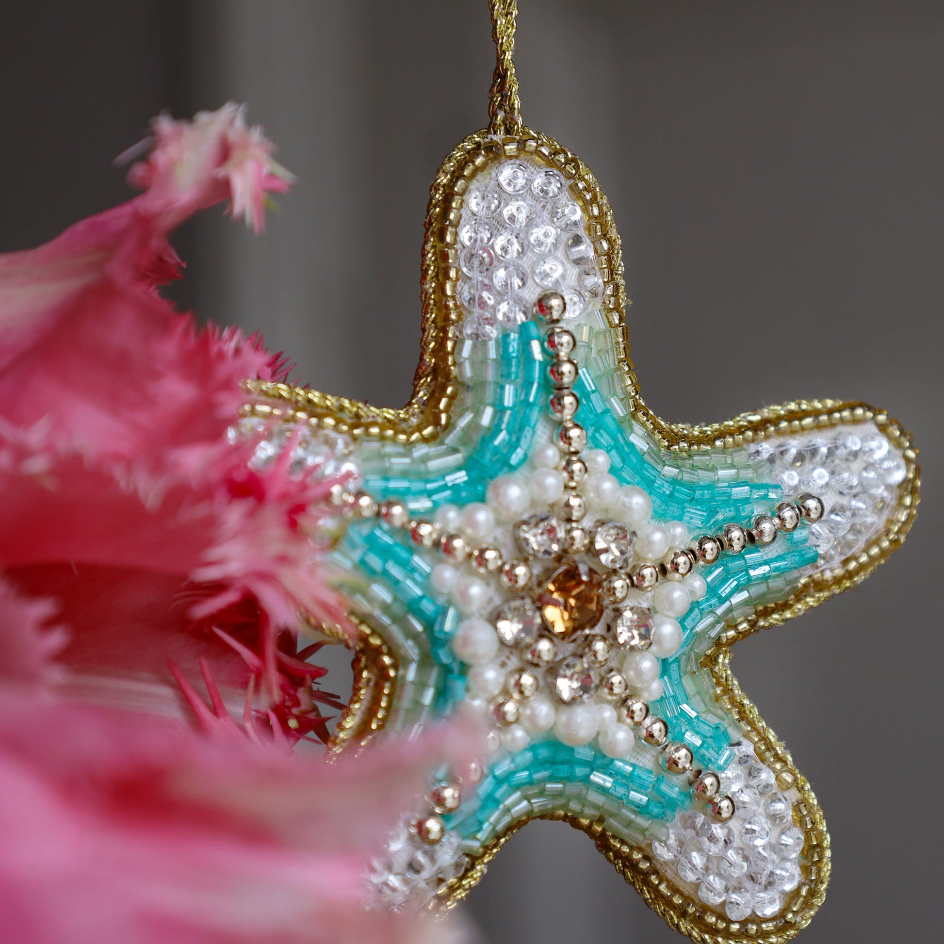 Decorative starfish ornament with beads and gemstones, close-up with pink flowers in the background.
