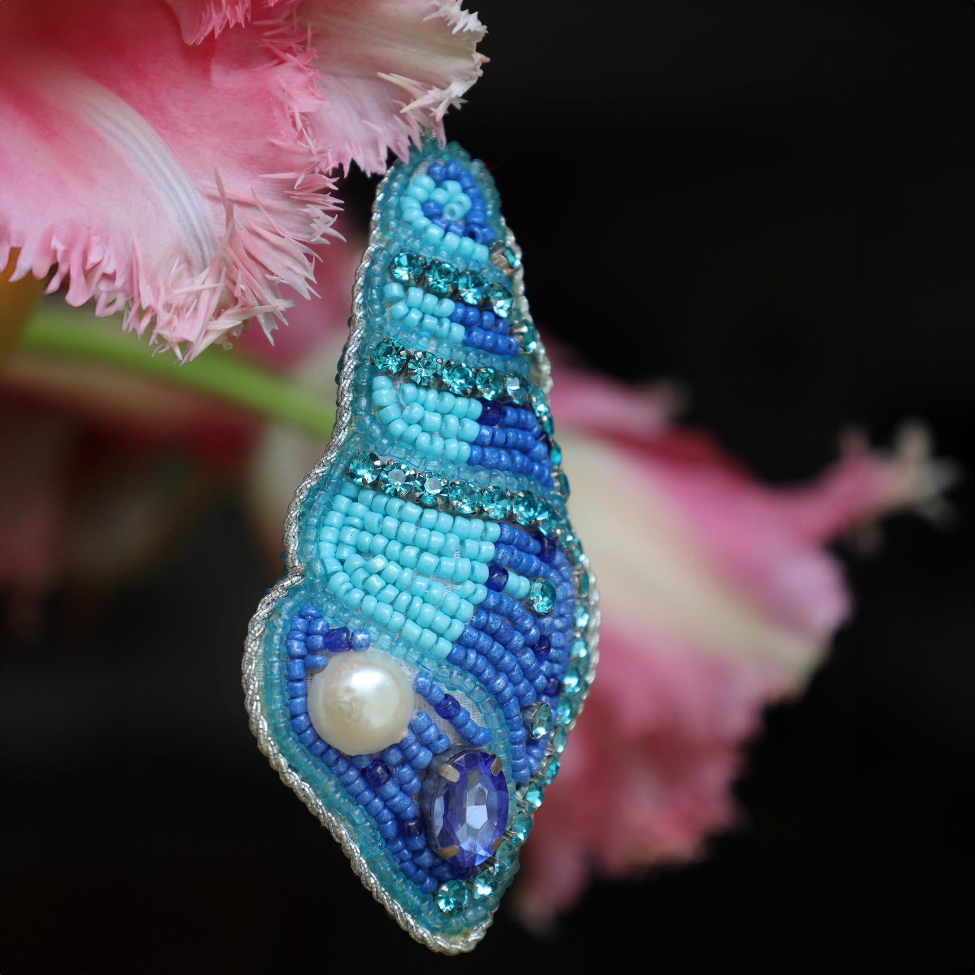 Blue and turquoise beaded shell with pearl on a pink flower background