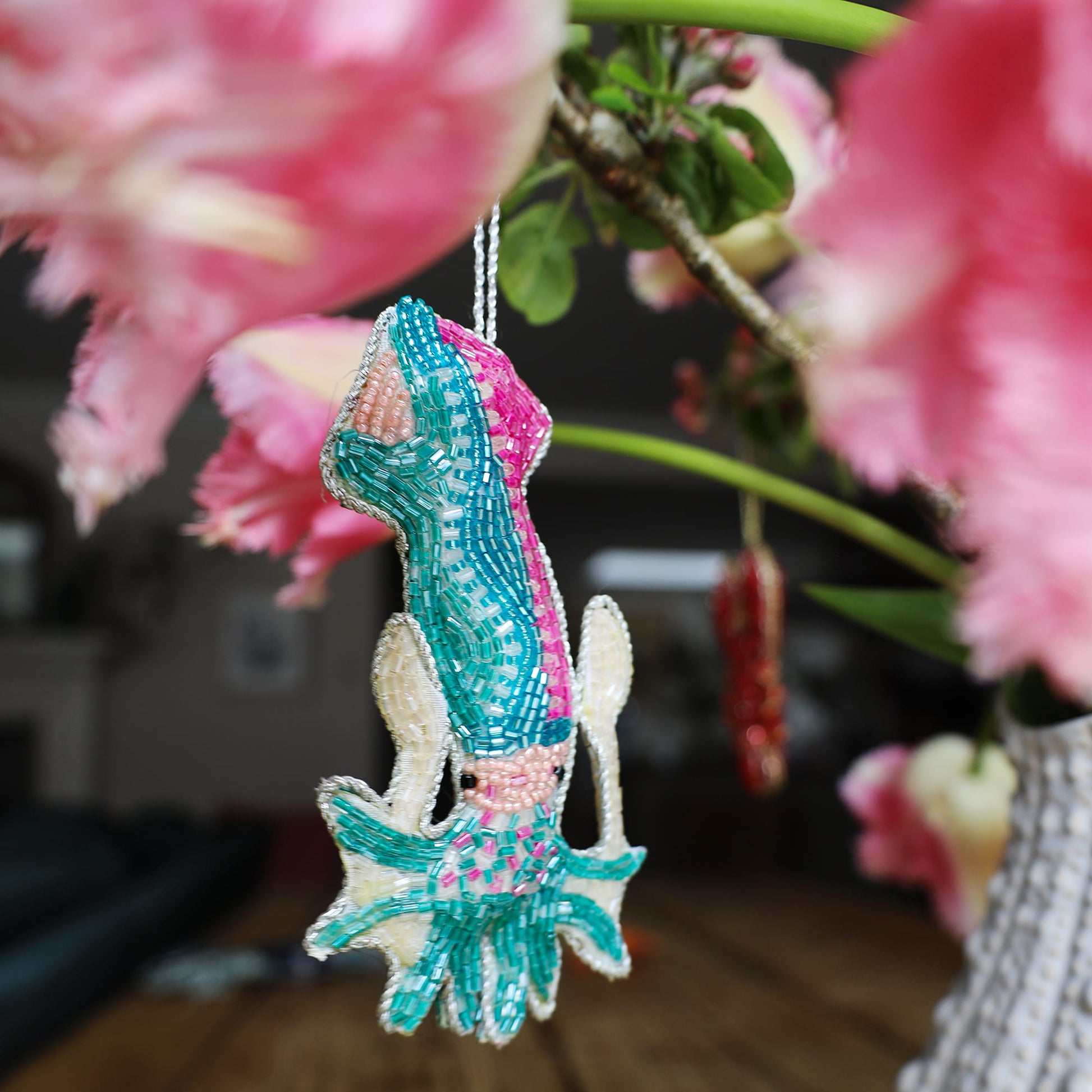 Decorative squid ornament with teal and pink patterns hanging against a blurred floral background.