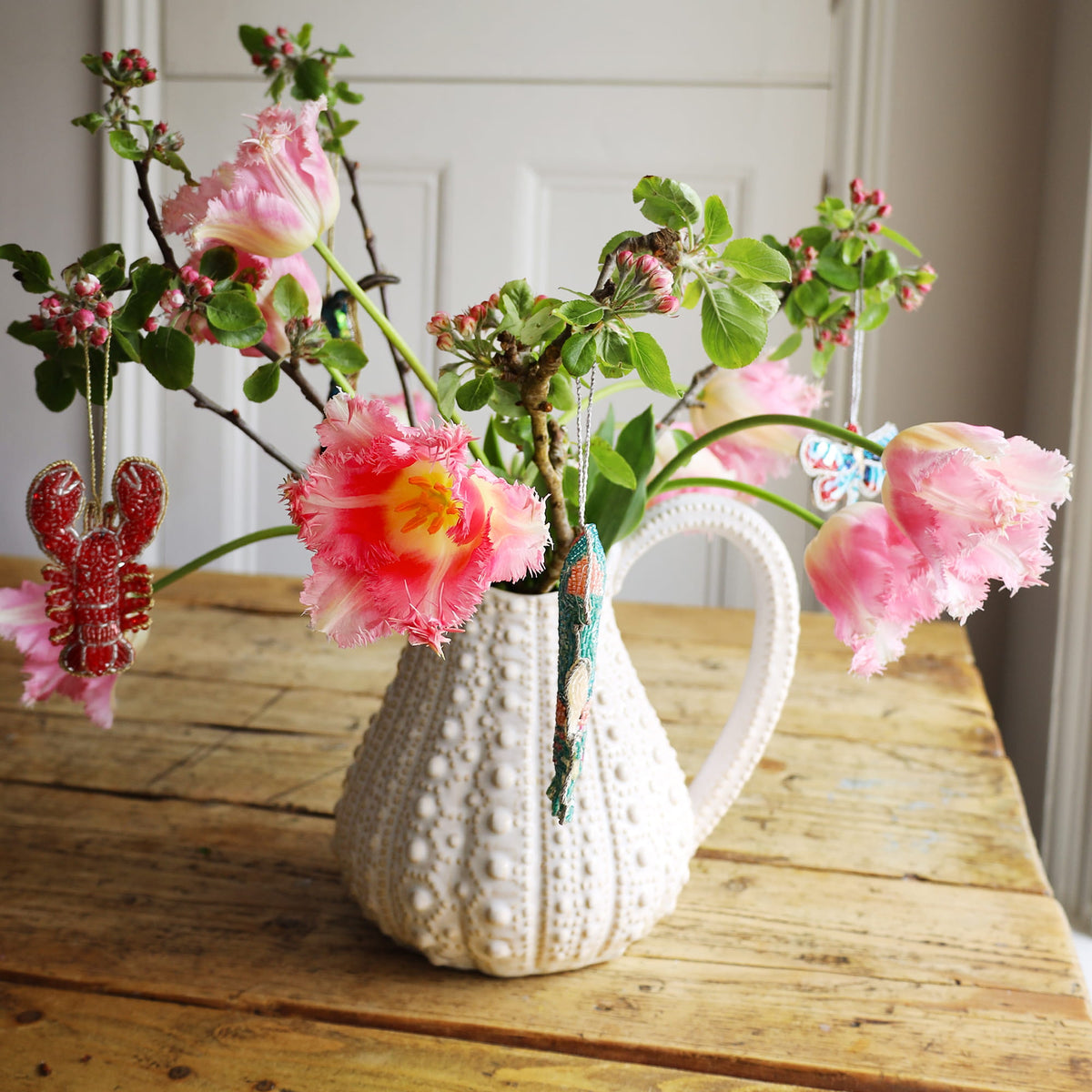 Decorative vase with pink flowers and green leaves on a wooden surface