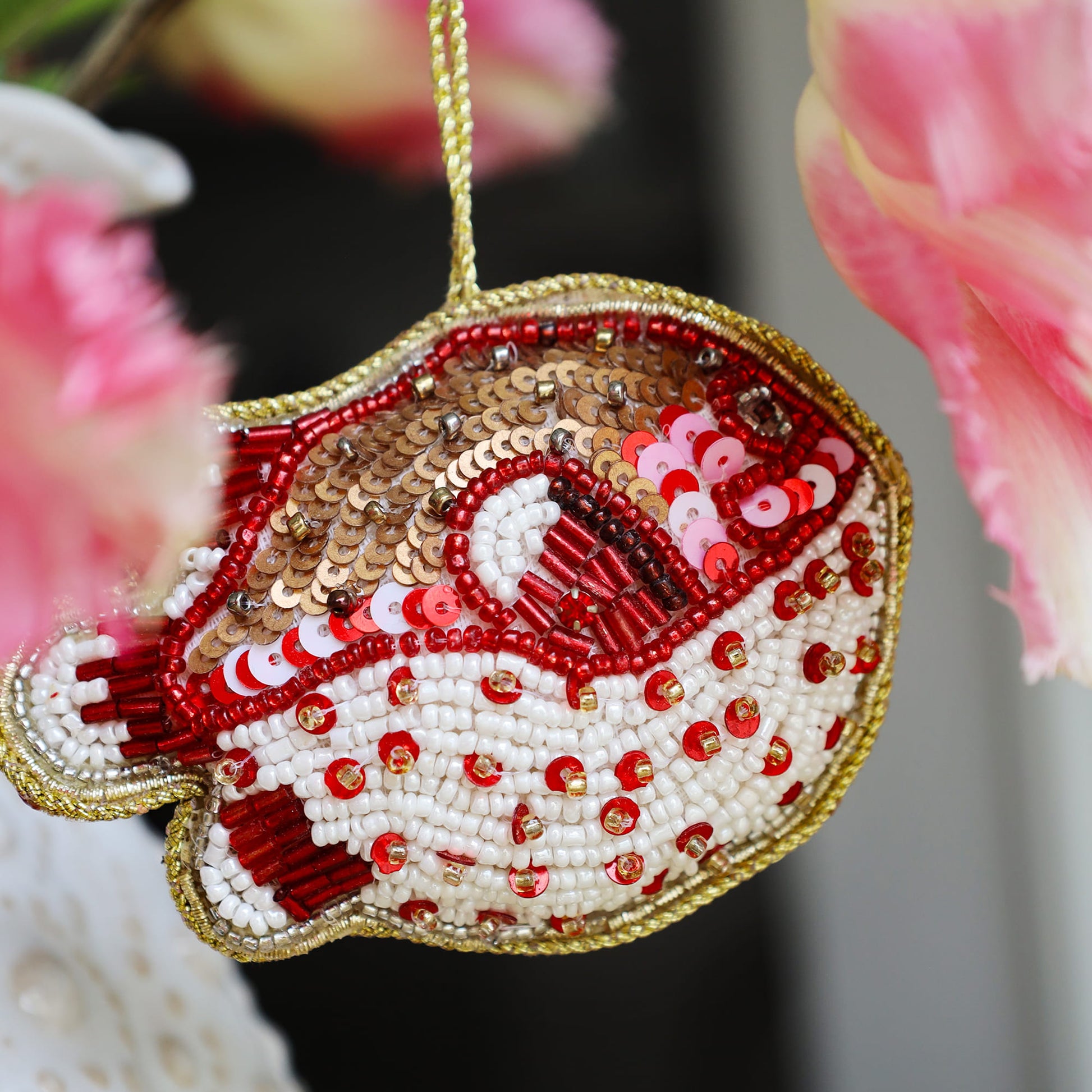 Decorative puffa fish ornament with red, white, and gold beads against a blurred floral background