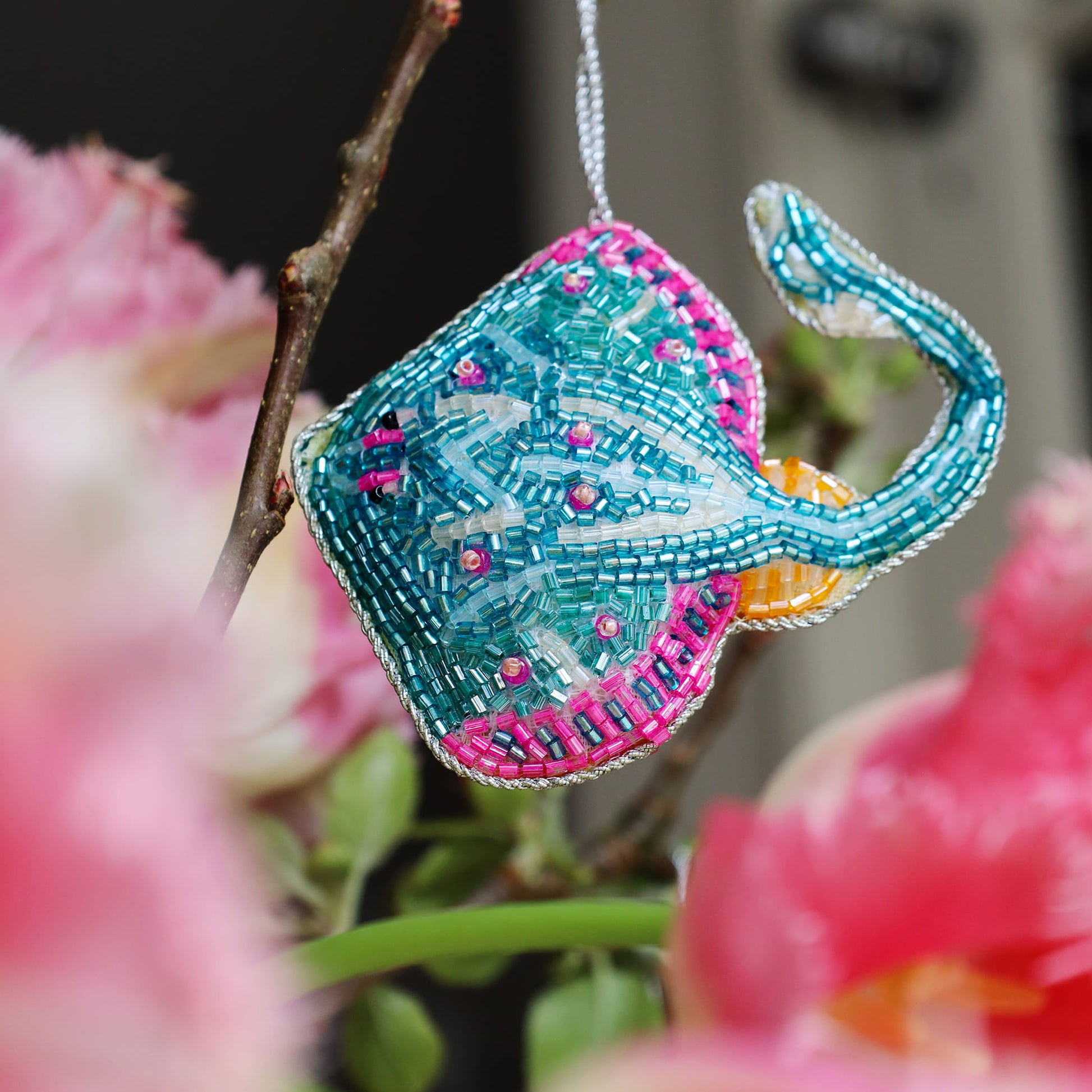 Decorative stingray ornament with teal and pink details hanging among pink flowers.