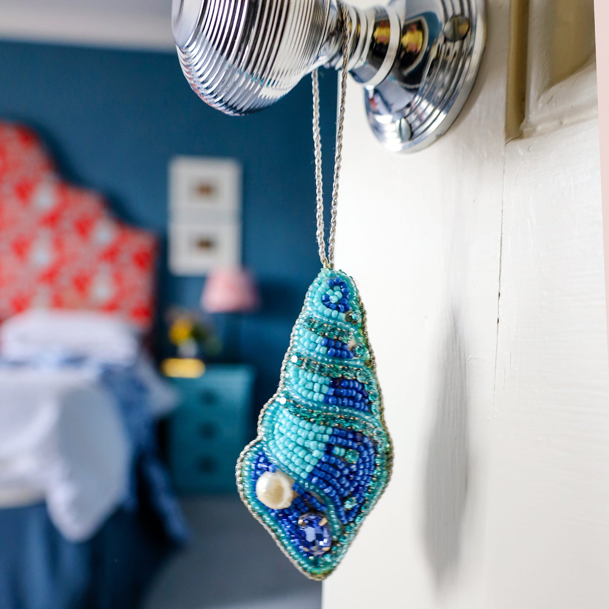 Decorative blue and green beaded shell ornament hanging from a curtain rod in a bedroom.