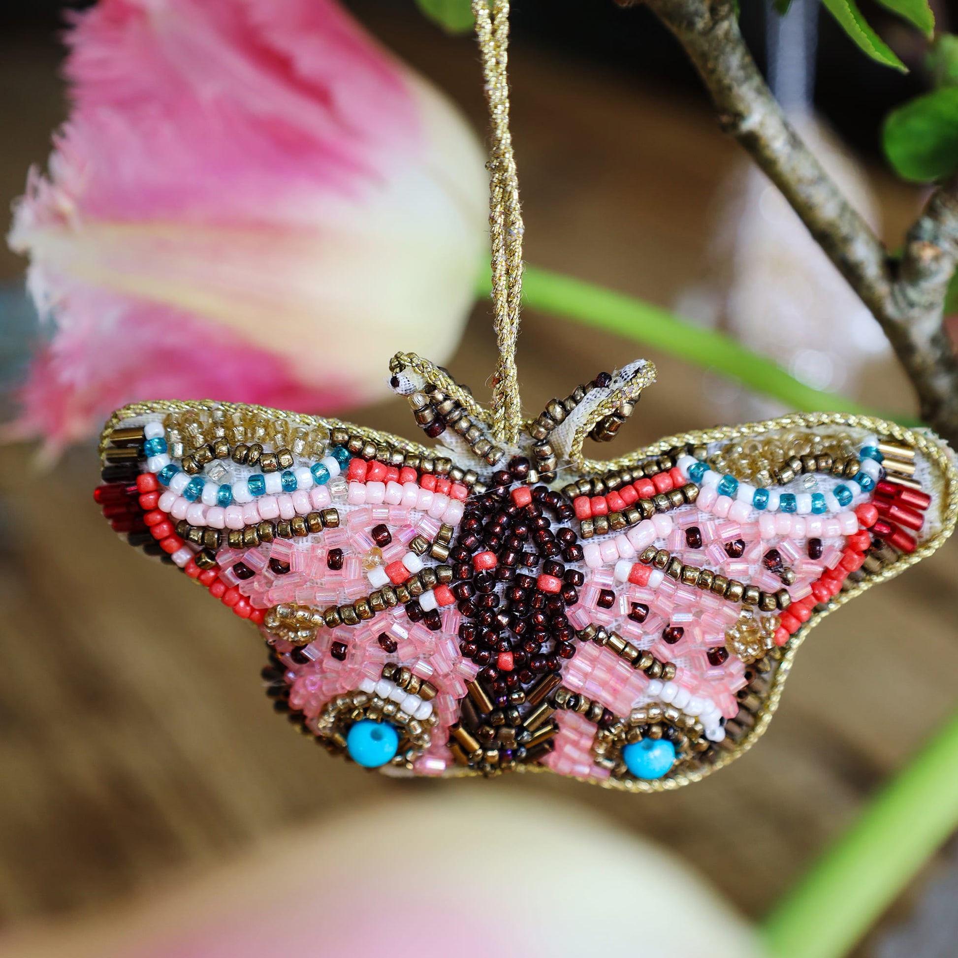 Beaded butterfly ornament with pink and gold colors on a blurred floral background