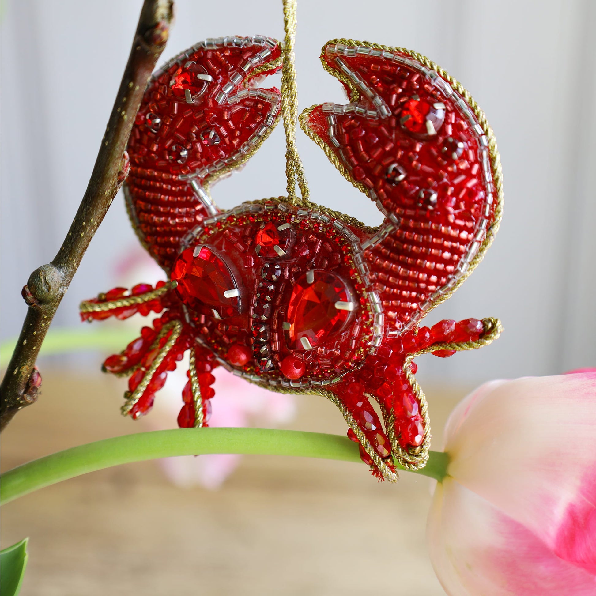 Red beaded crab ornament hanging on a branch with a blurred background