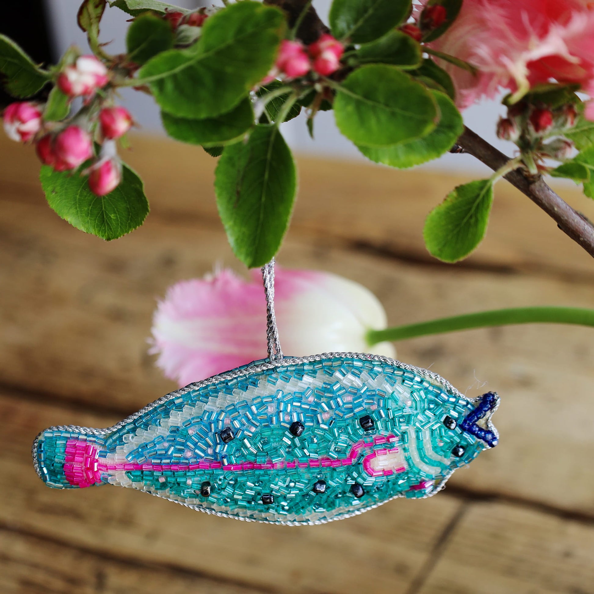Decorative fish ornament with beaded details on a wooden surface with flowers in the background