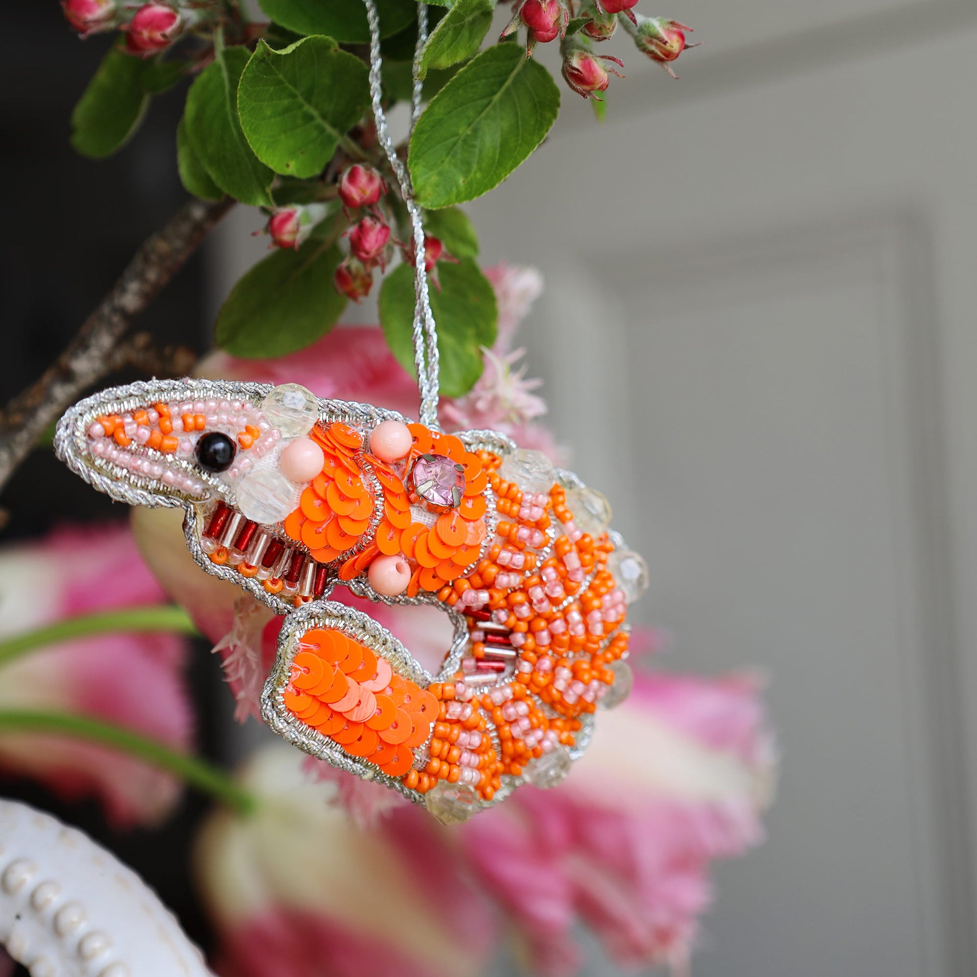 Decorative prawn ornament with orange and silver beads hanging against a blurred floral background