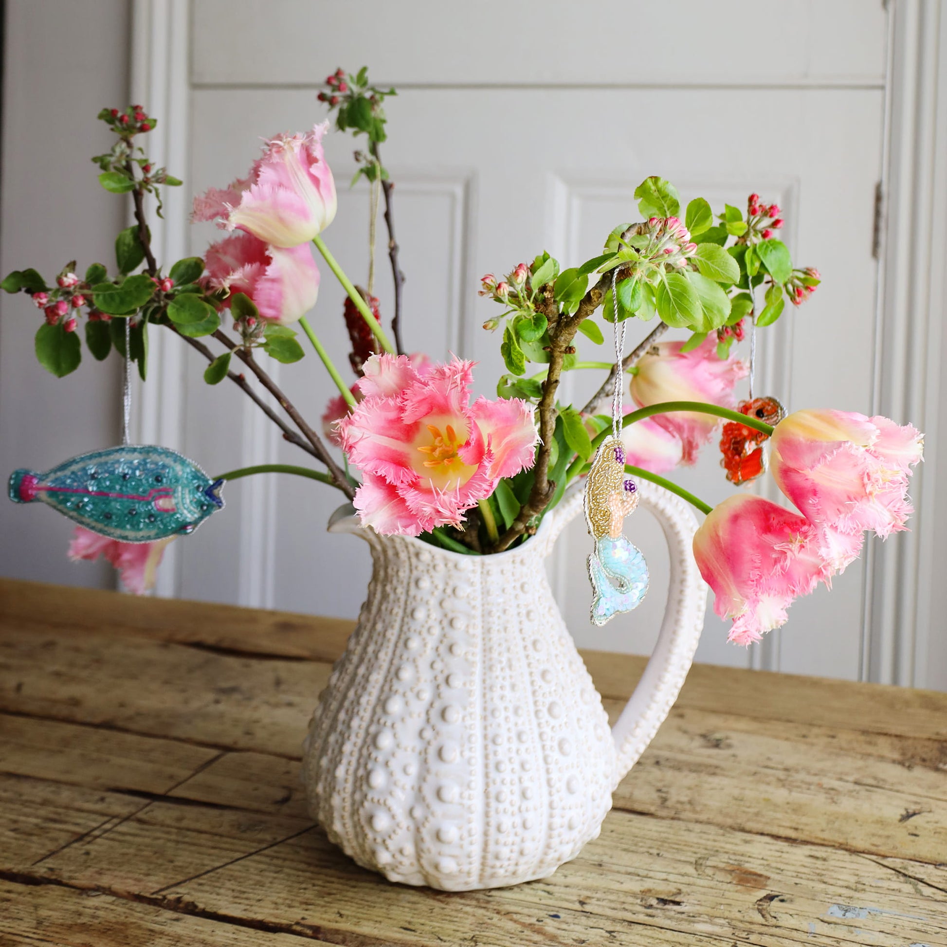White textured vase with pink flowers on a wooden surface