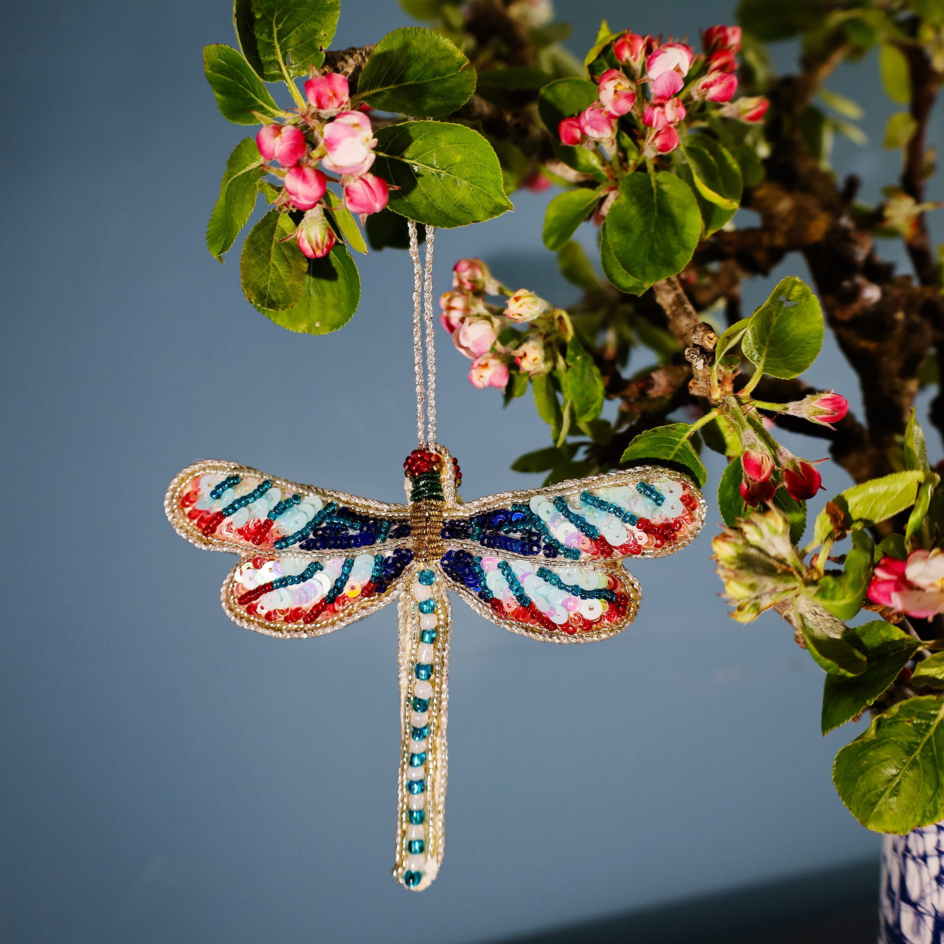 Colorful dragonfly ornament hanging from a tree branch with flowers.
