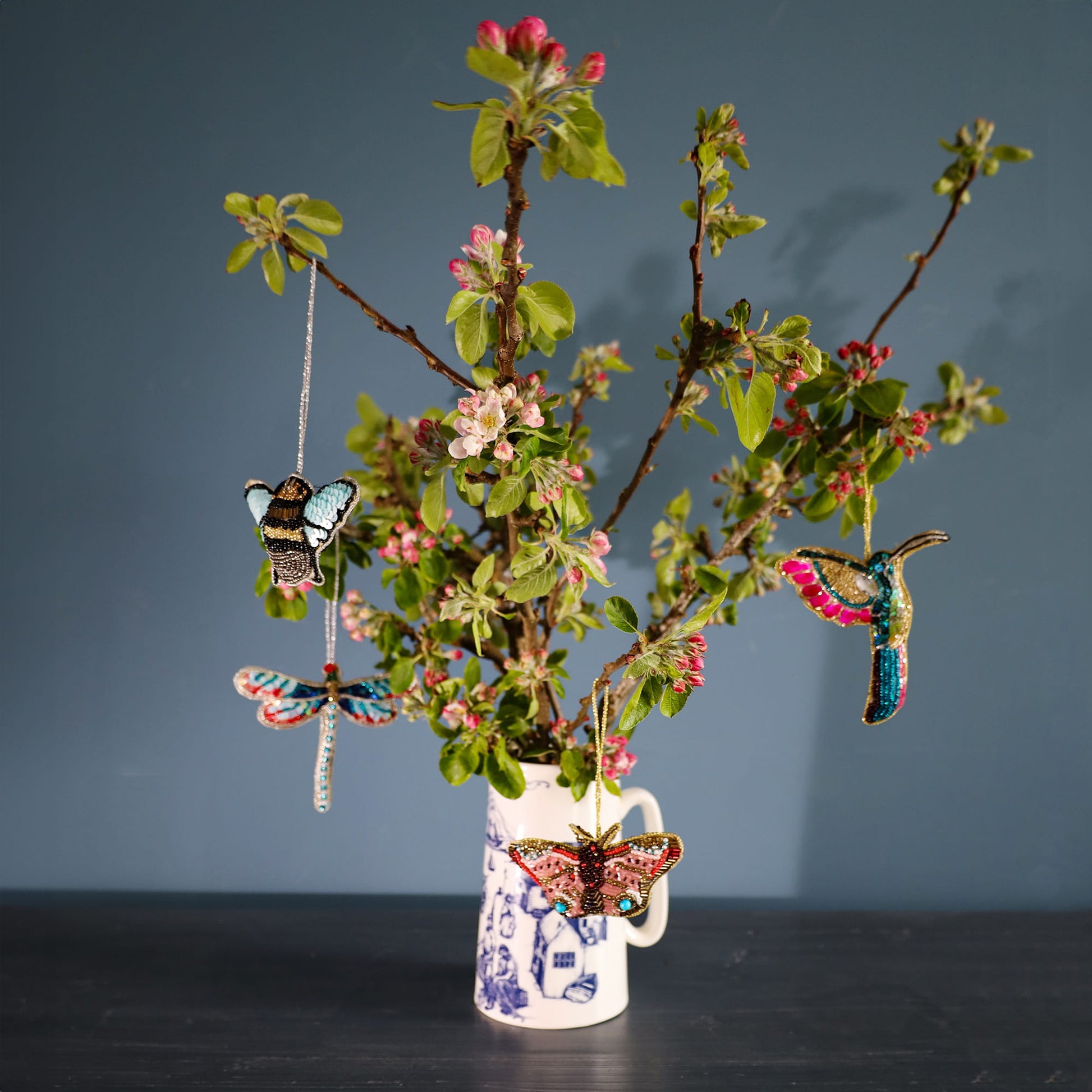 Decorative vase with floral branches and hanging butterfly ornaments against a dark background