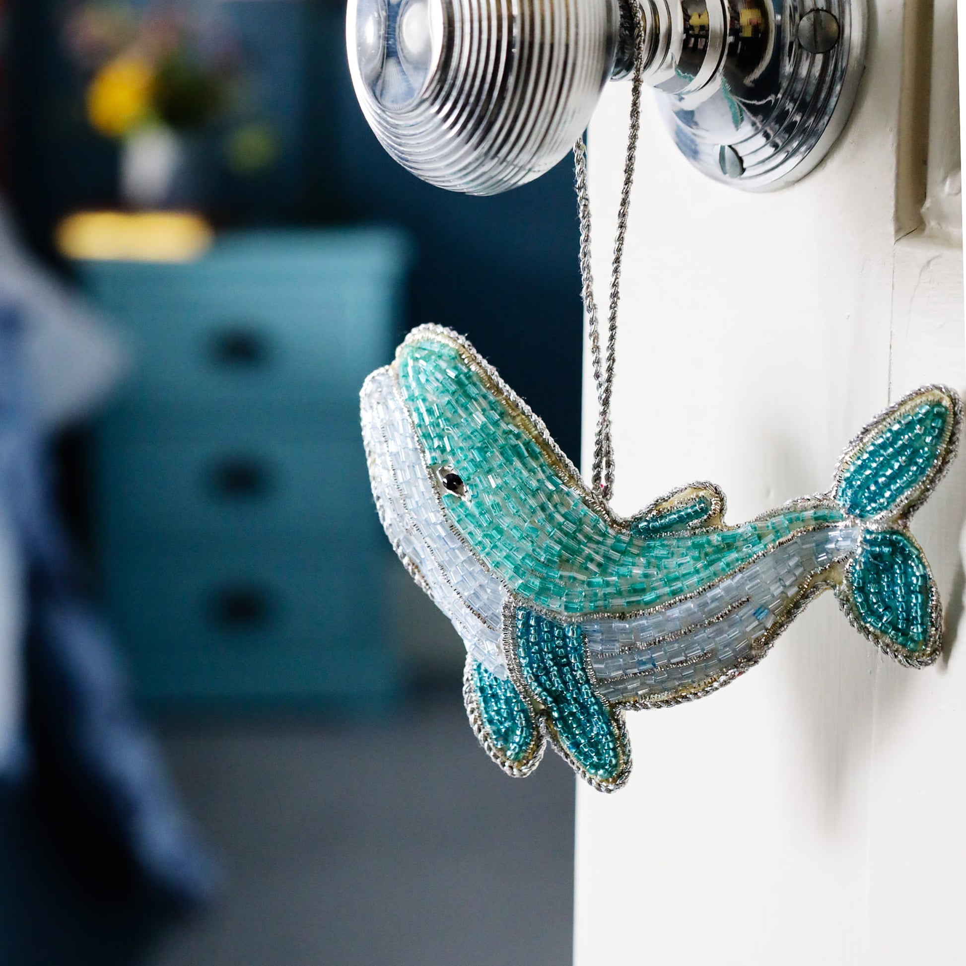 Decorative beaded whale ornament hanging on a hook with a blurred background