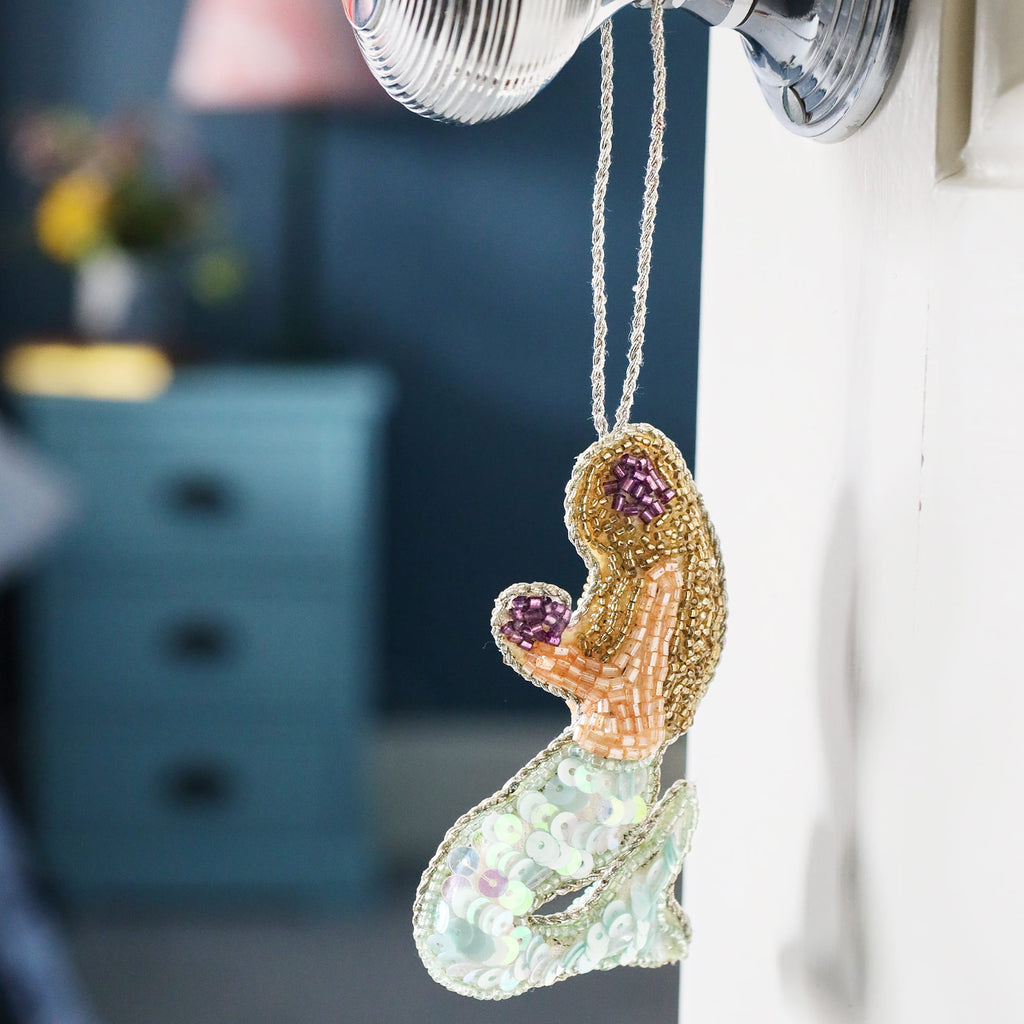Decorative mermaid tail ornament hanging on a hook with a blurred room background.