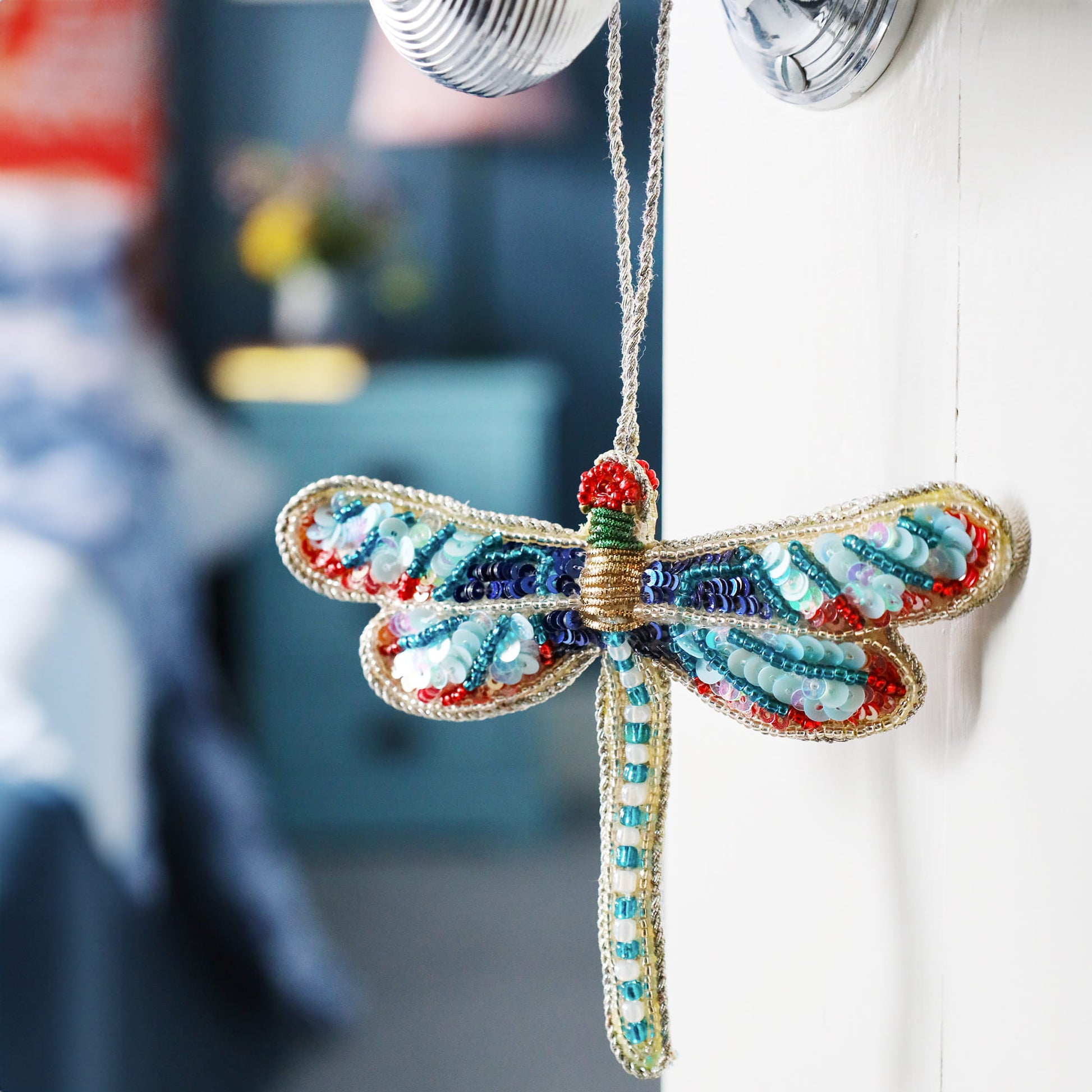 Colorful beaded dragonfly ornament hanging on a wall.
