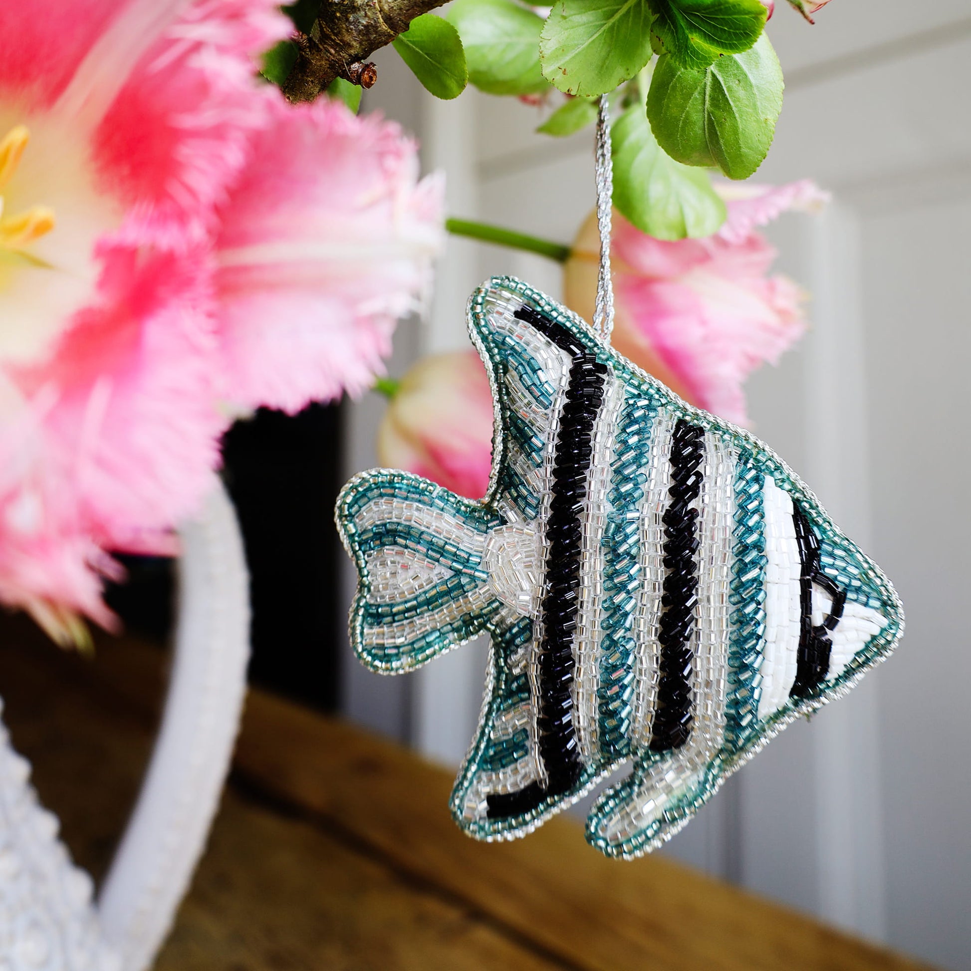 Decorative fish ornament with beaded details hanging against a floral background