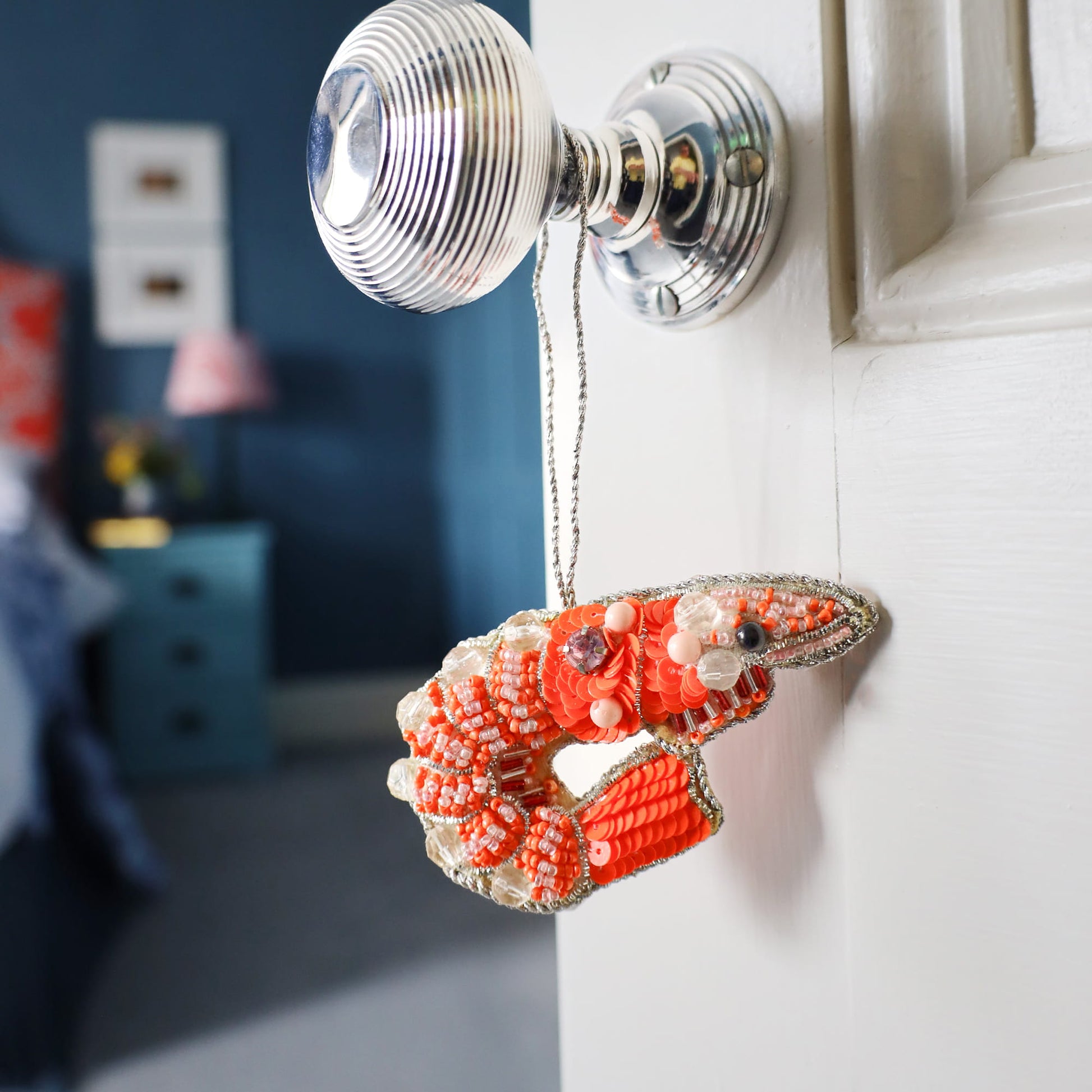 Decorative prawn ornament hanging on a door handle with a blurred room background