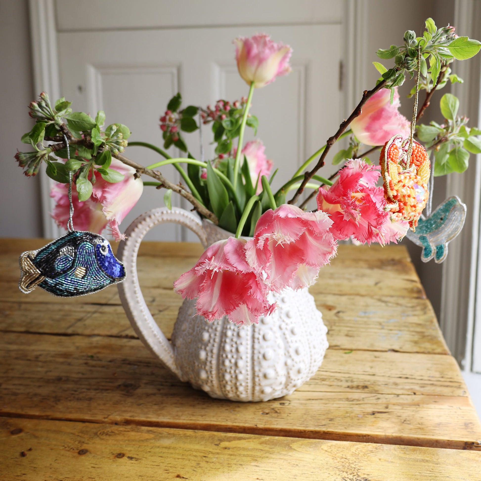 Decorative urchin jug with pink flowers on a wooden table and beaded decorations.