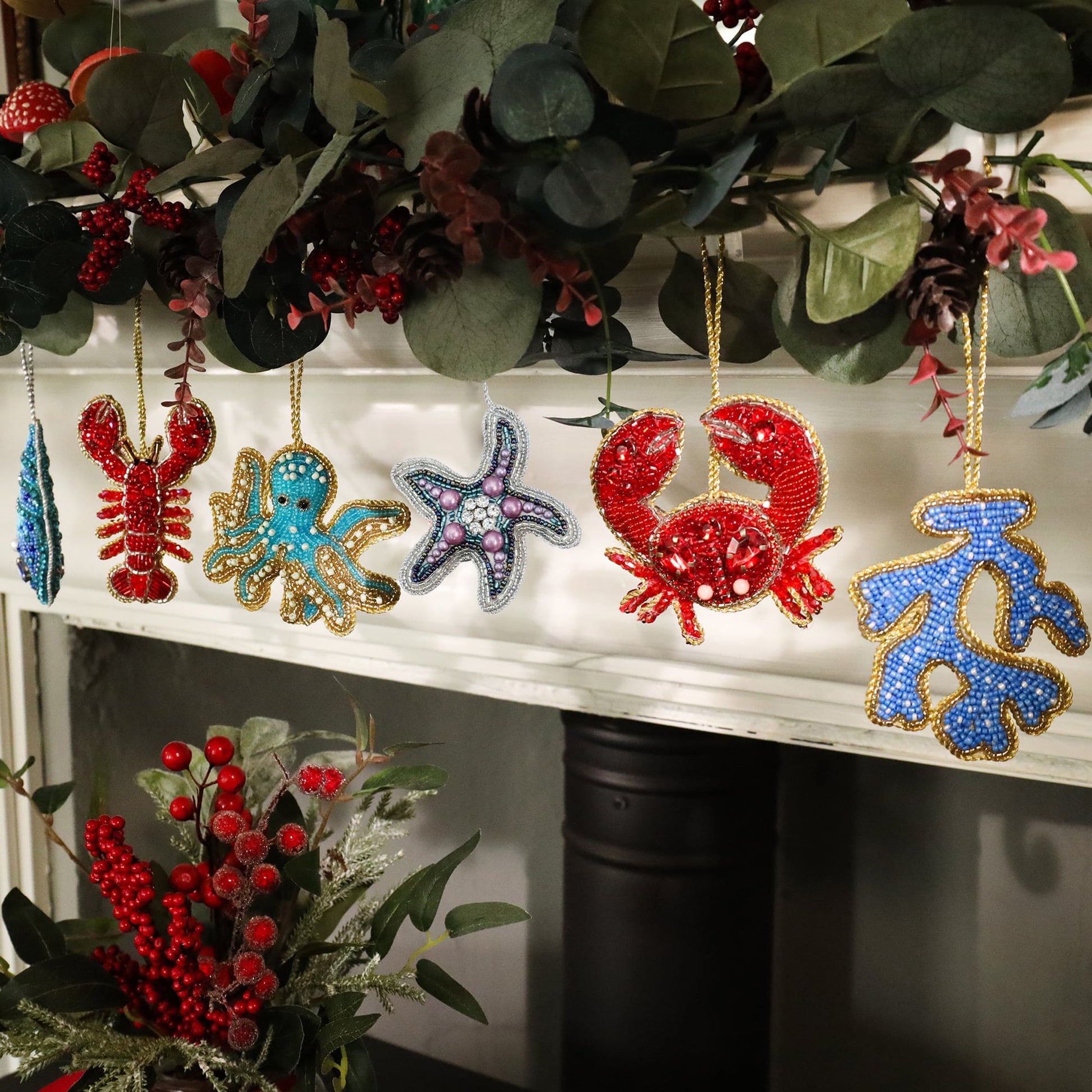 Decorative Christmas ornaments shaped like a lobster, octopus, and starfish on a mantel with greenery.