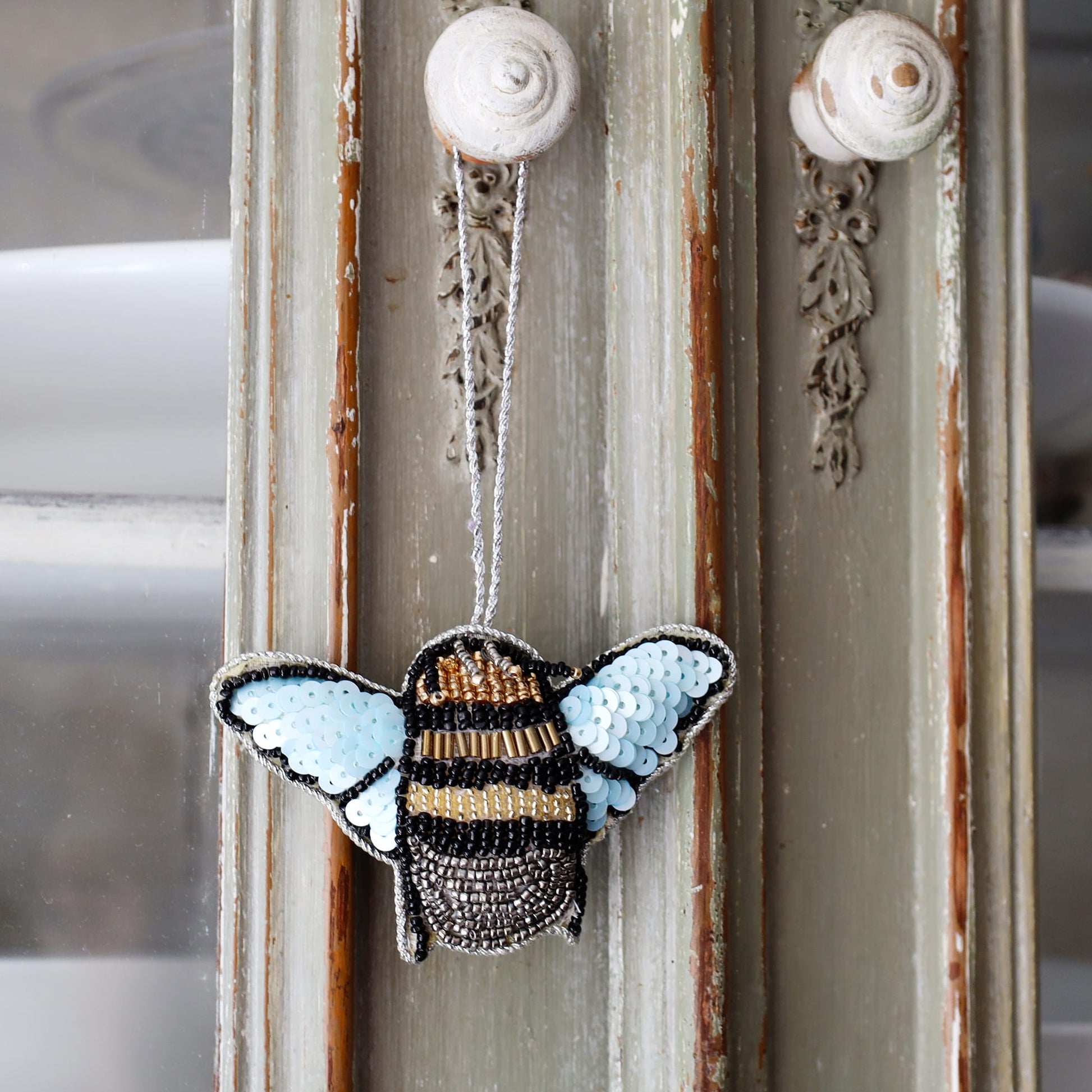 Decorative bee ornament with sequin wings hanging on a door.