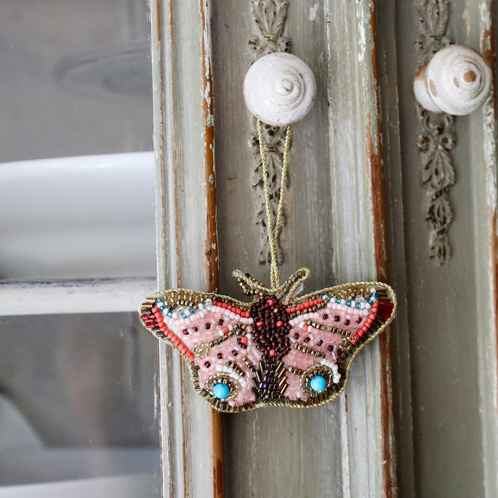 Decorative butterfly ornament with beads hanging on a textured wall.
