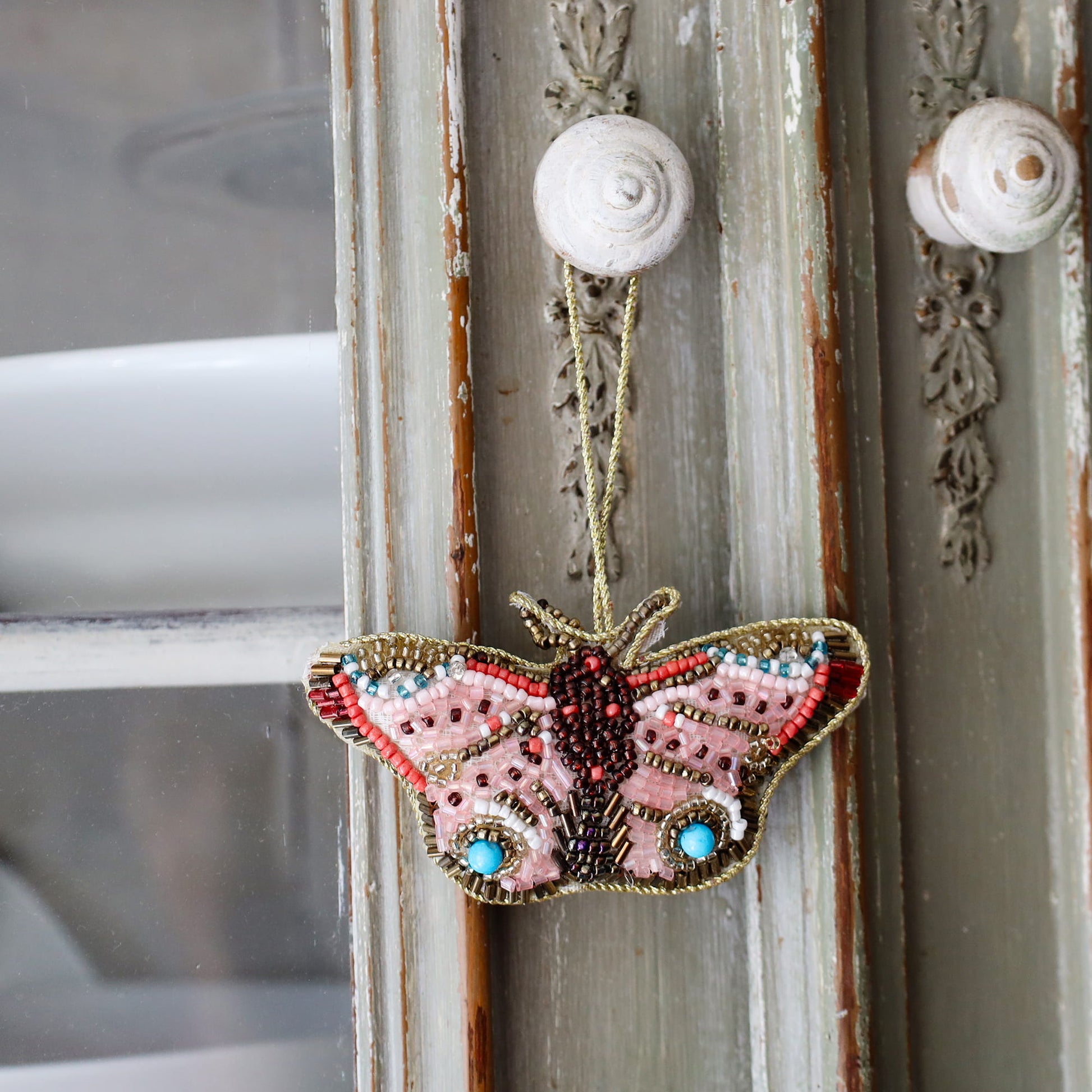 Decorative butterfly ornament with beads hanging on a textured wall.