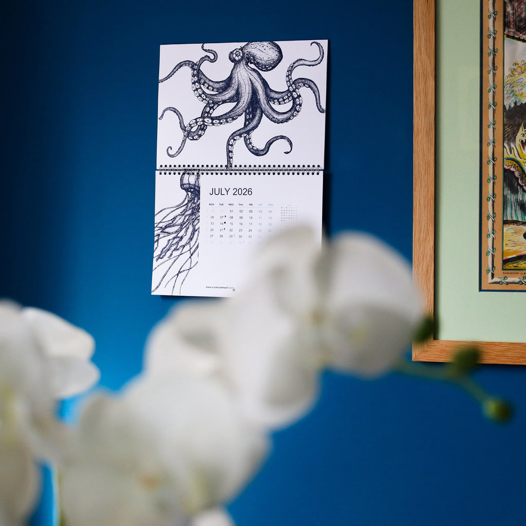 Cream Cornwall 2026 wall calendar open to July with octopus illustration on blue wall.