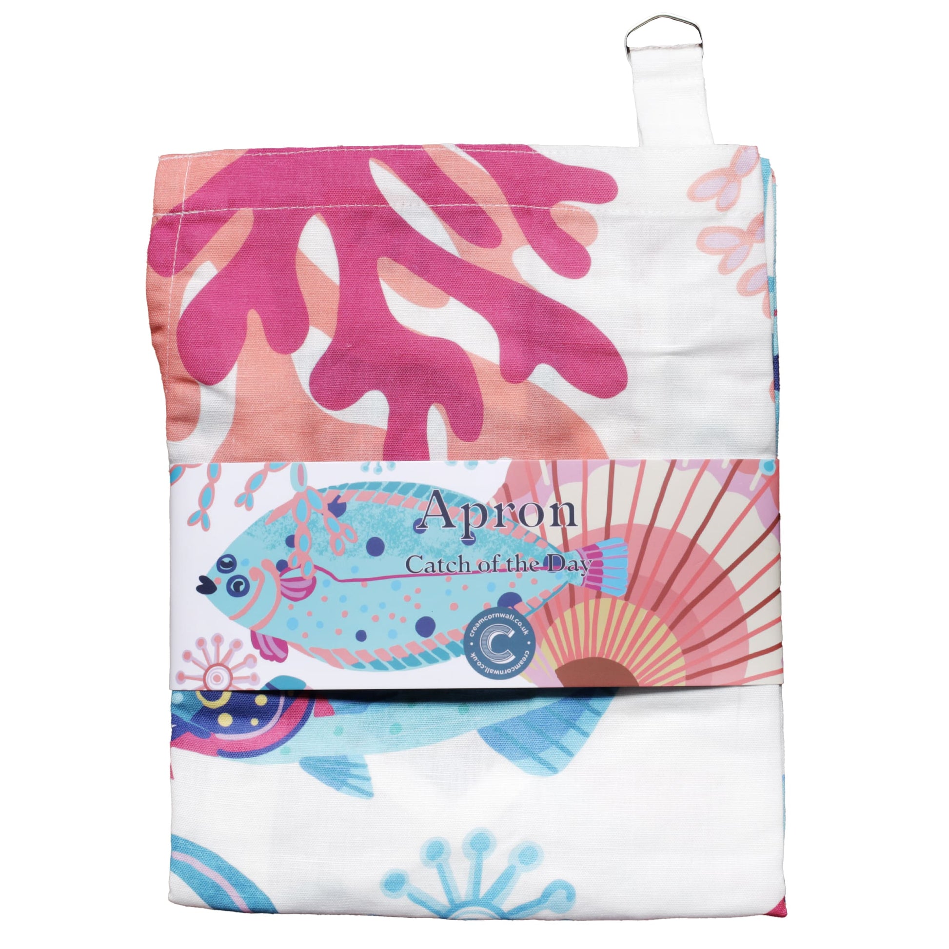 Folded cotton apron with a vibrant marine-themed print featuring coral, a flat fish, and seashells in pink, turquoise, and blue on a white background. The apron is wrapped with a branded label that reads 'Apron – Catch of the Day,' showcasing part of the sea-inspired design.