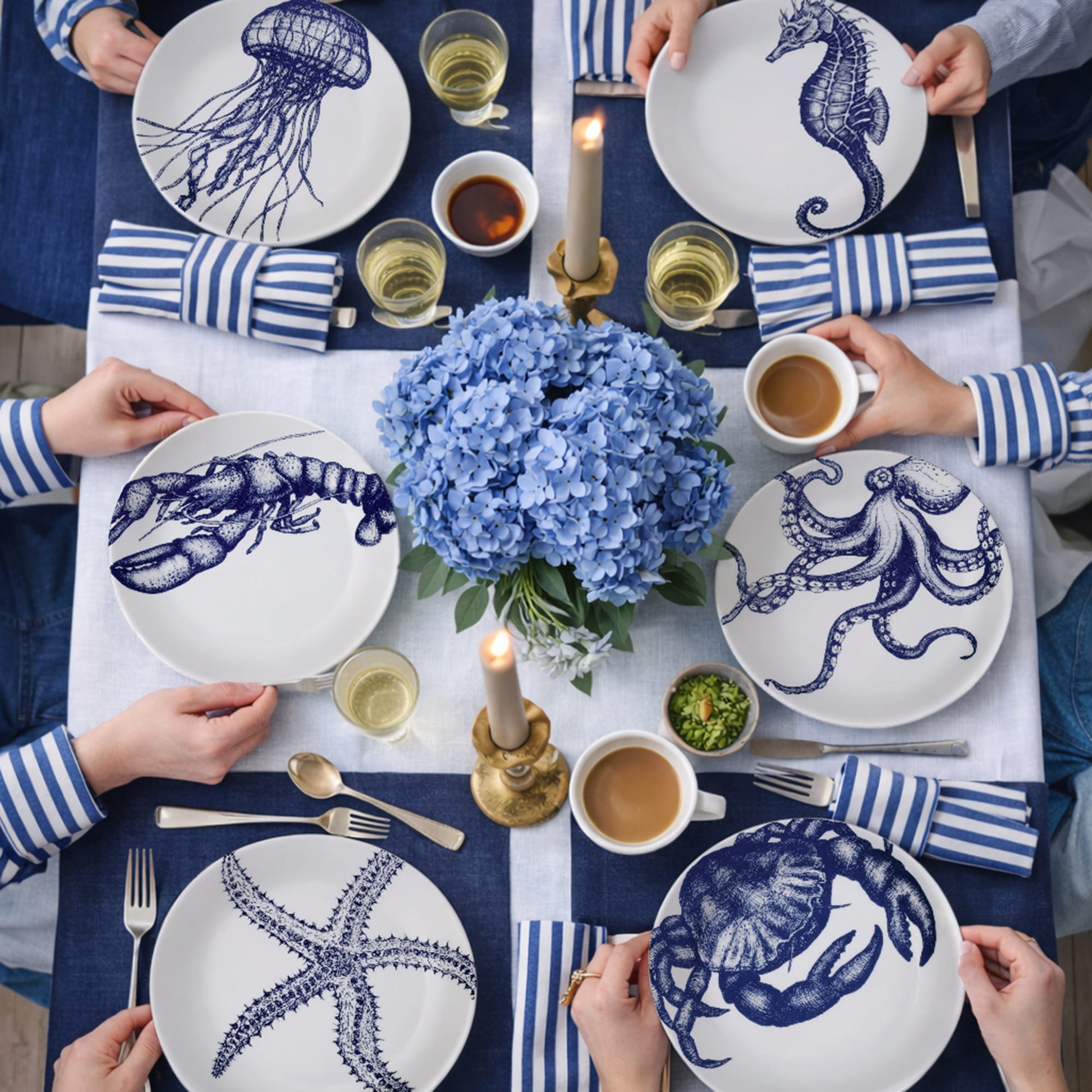 Table setting with blue and white plates featuring sea creature designs, surrounded by people holding cups.