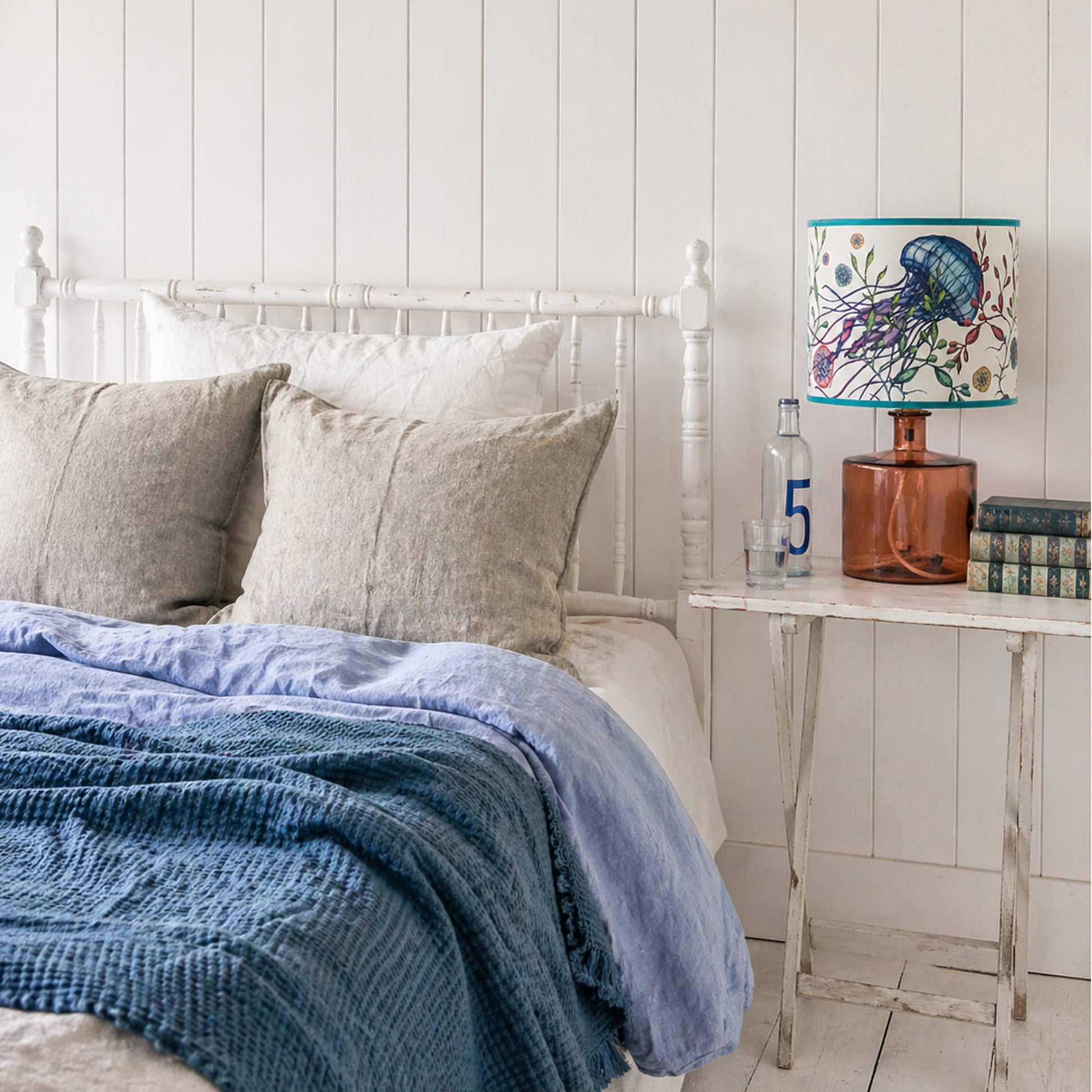 Bedroom with a bed featuring blue bedding and gray pillows, next to a nightstand with a decorative lamp.