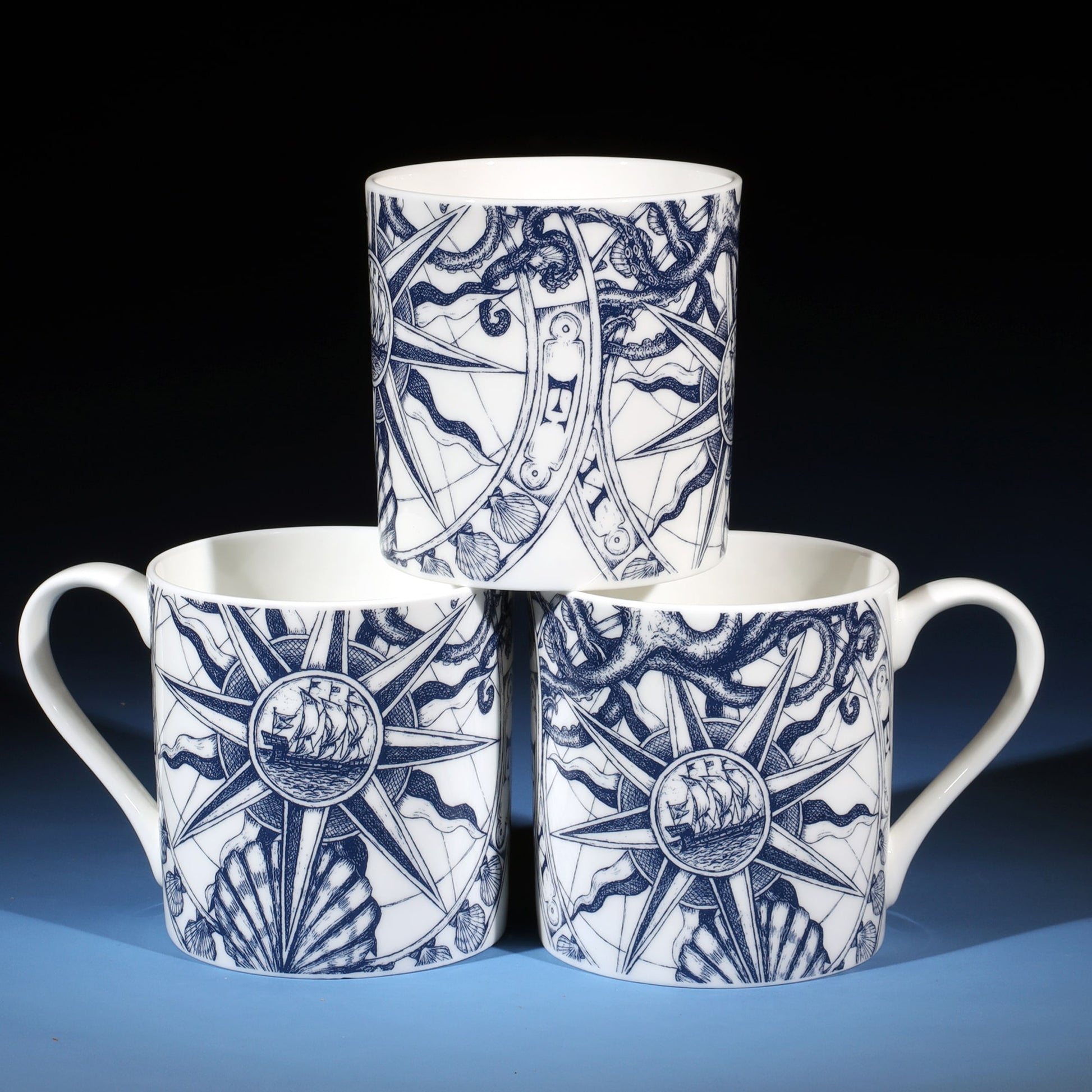 Stack of three Comnpass Mugs showing front and back designs.