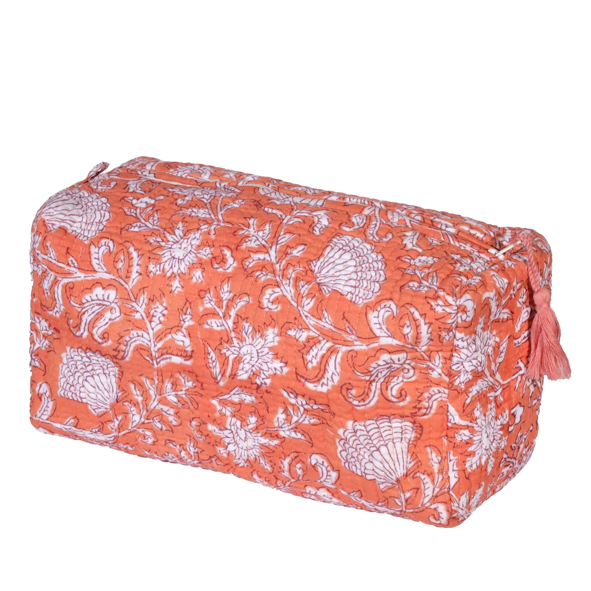 A rectangular coral-colored wash bag with a white floral and seashell block print design, featuring a quilted texture and a matching coral tassel on the zipper.