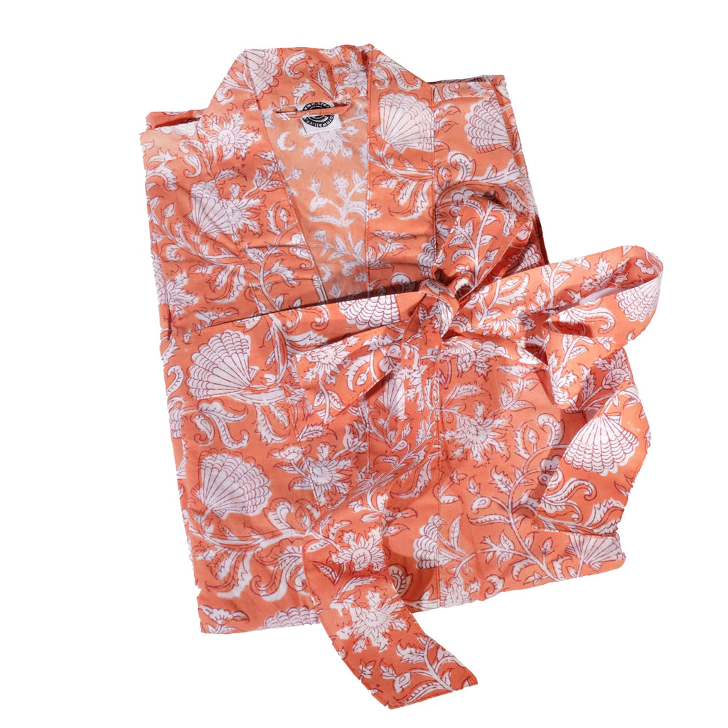 A folded coral-colored dressing gown featuring a white floral and seashell block print design, tied neatly with its matching belt on a plain white background.