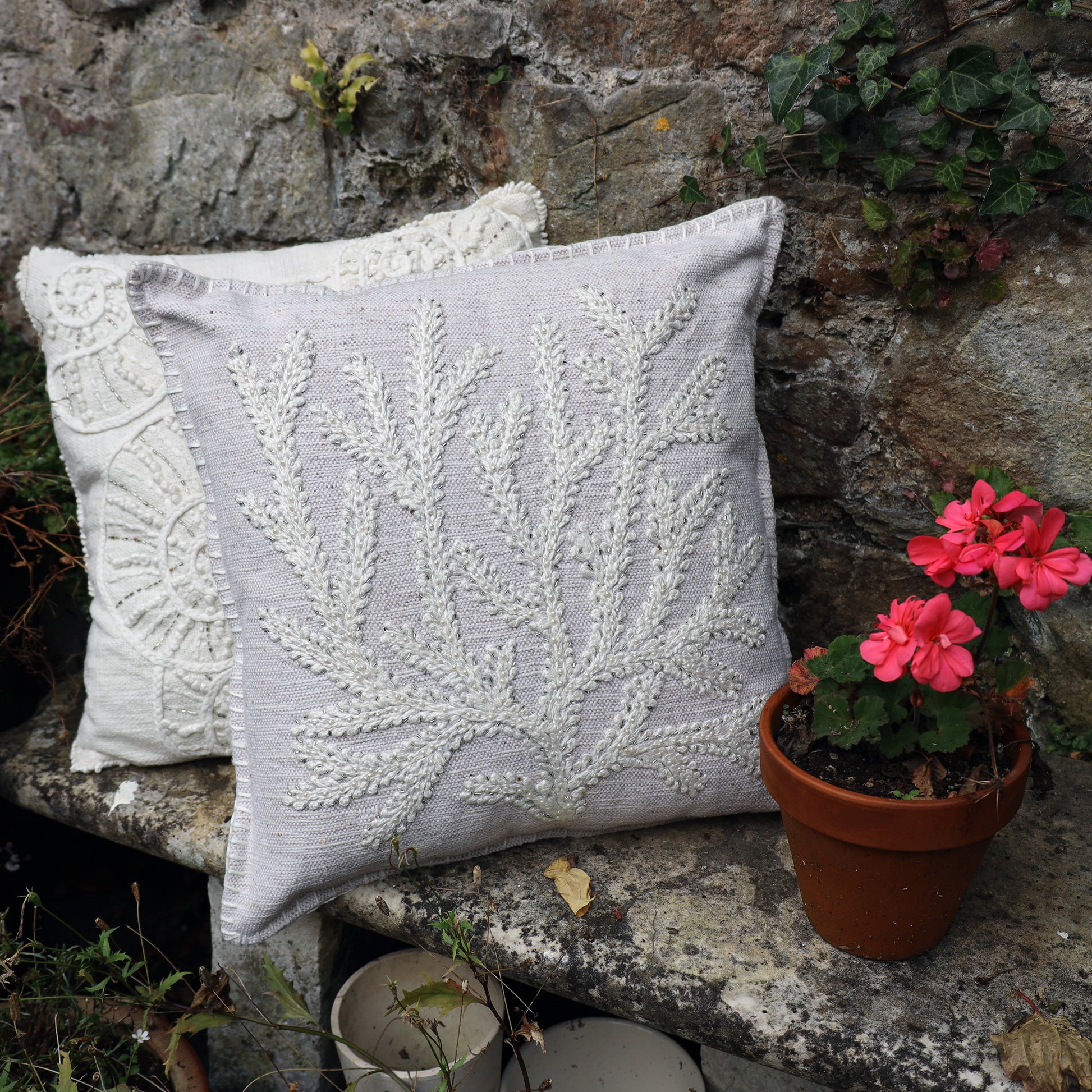 Decorative pillow with coral on a stone surface with a potted plant.