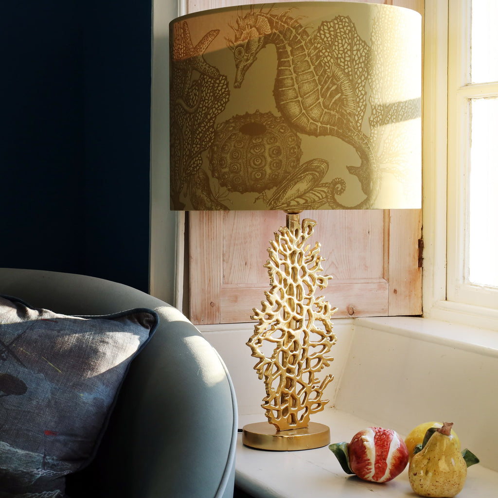 Decorative gold coral lamp with seahorse design lampshade on a table next to a window