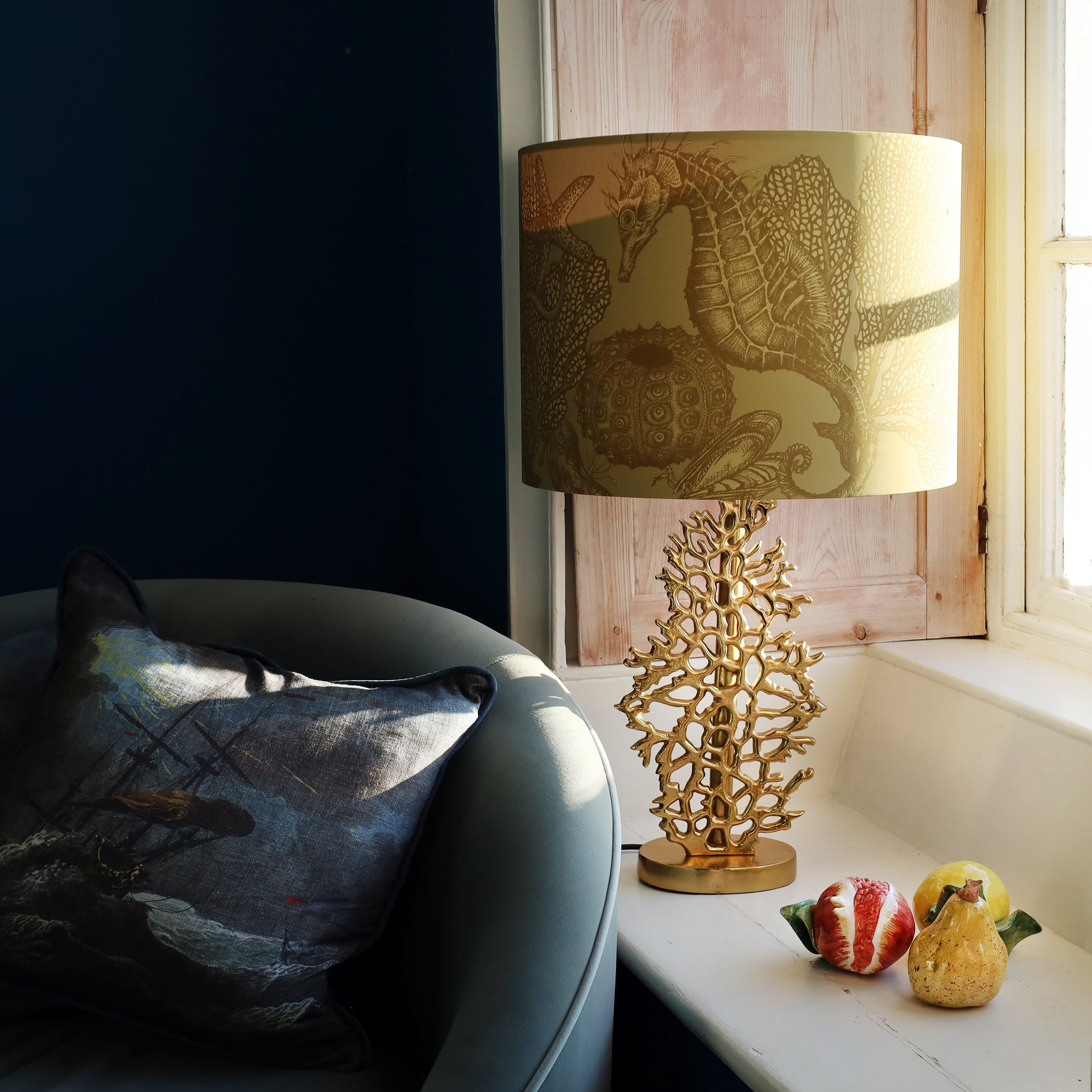 Decorative gold coral lamp base with seahorse lampshade design on a windowsill next to a sofa.