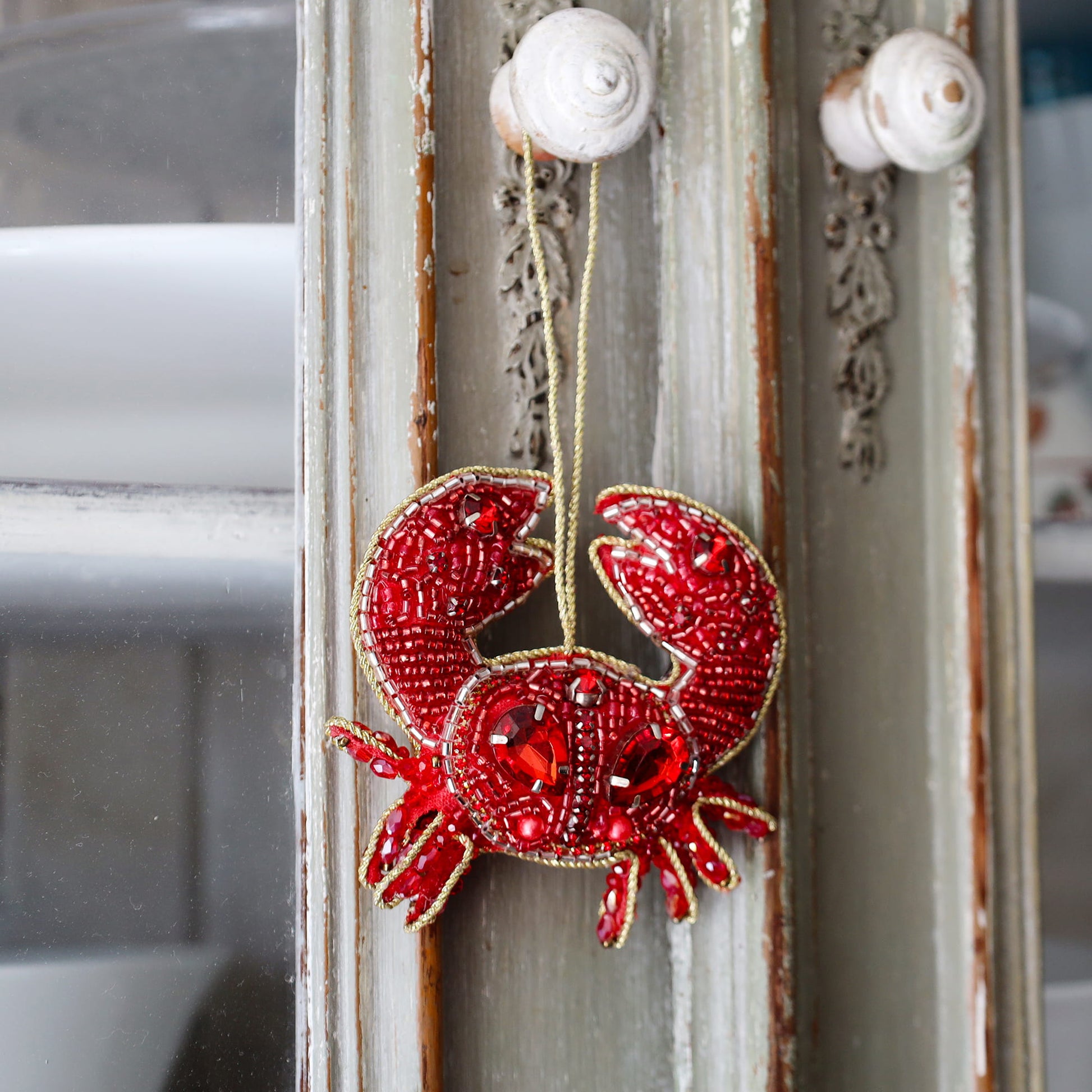 Red crab ornament hanging on a decorative door with white knobs.