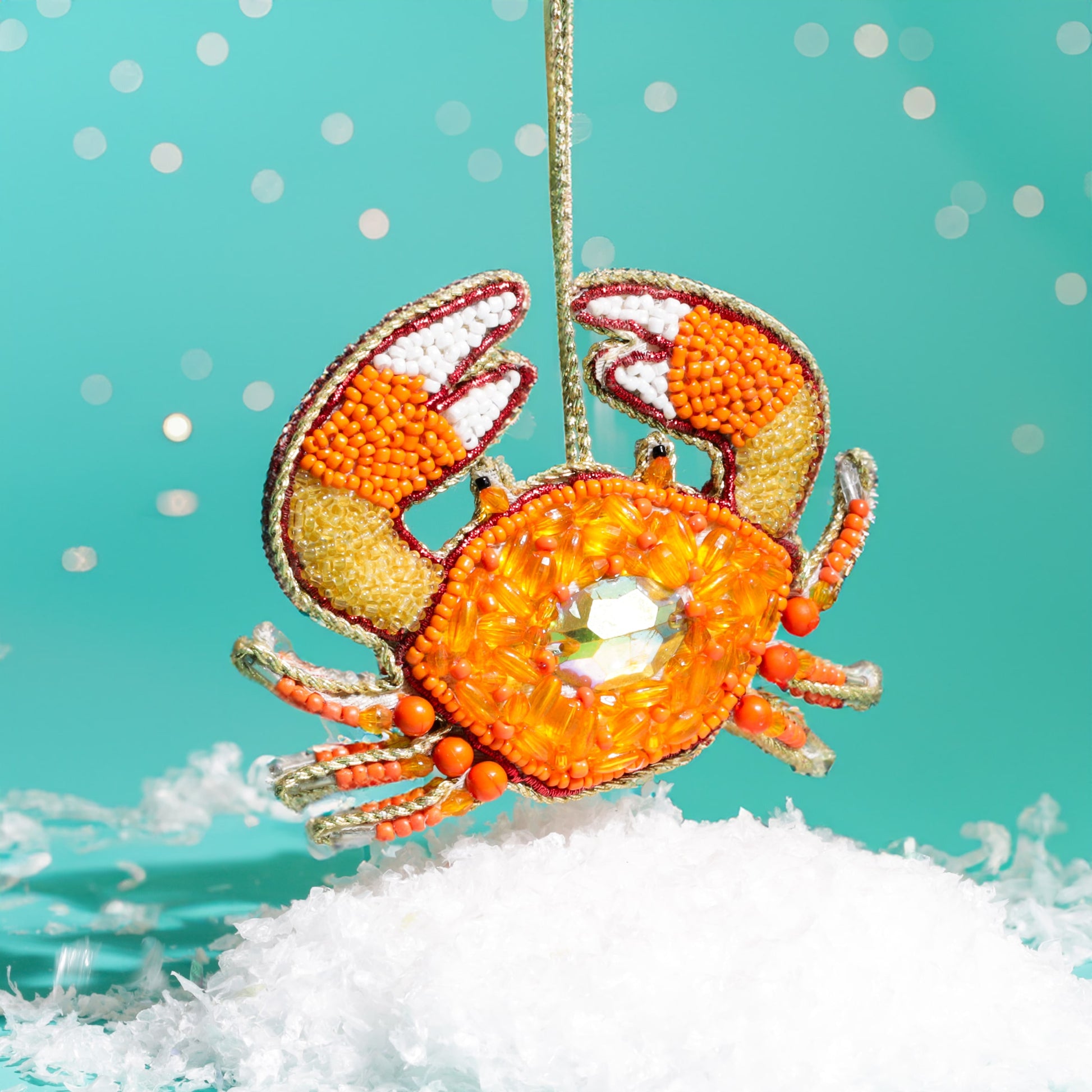 Decorative crab ornament with orange and white details on a turquoise background