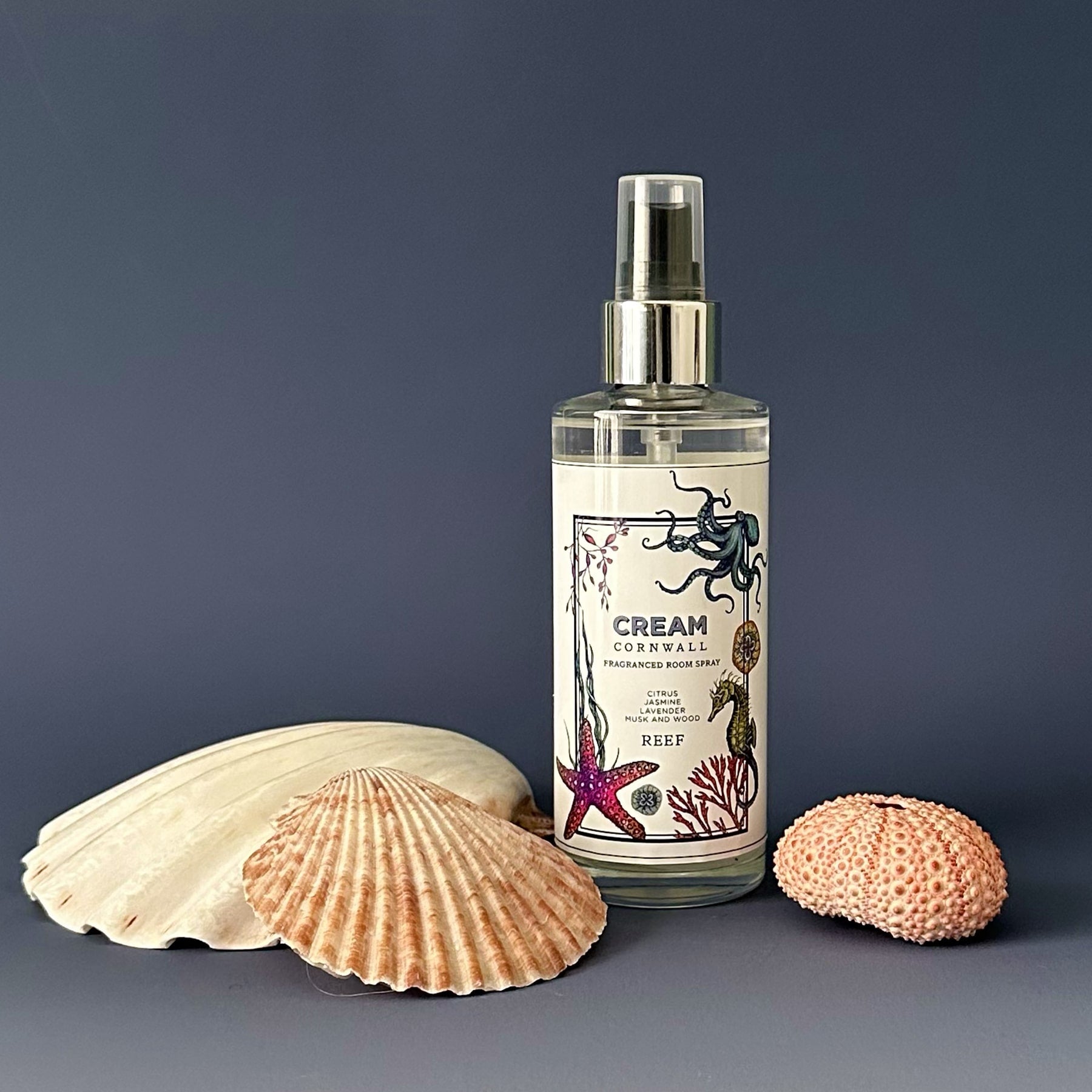 Fragrance Room Spray glass bottle with atomiser top,Reef logo on label,next to three shells of various sizes.