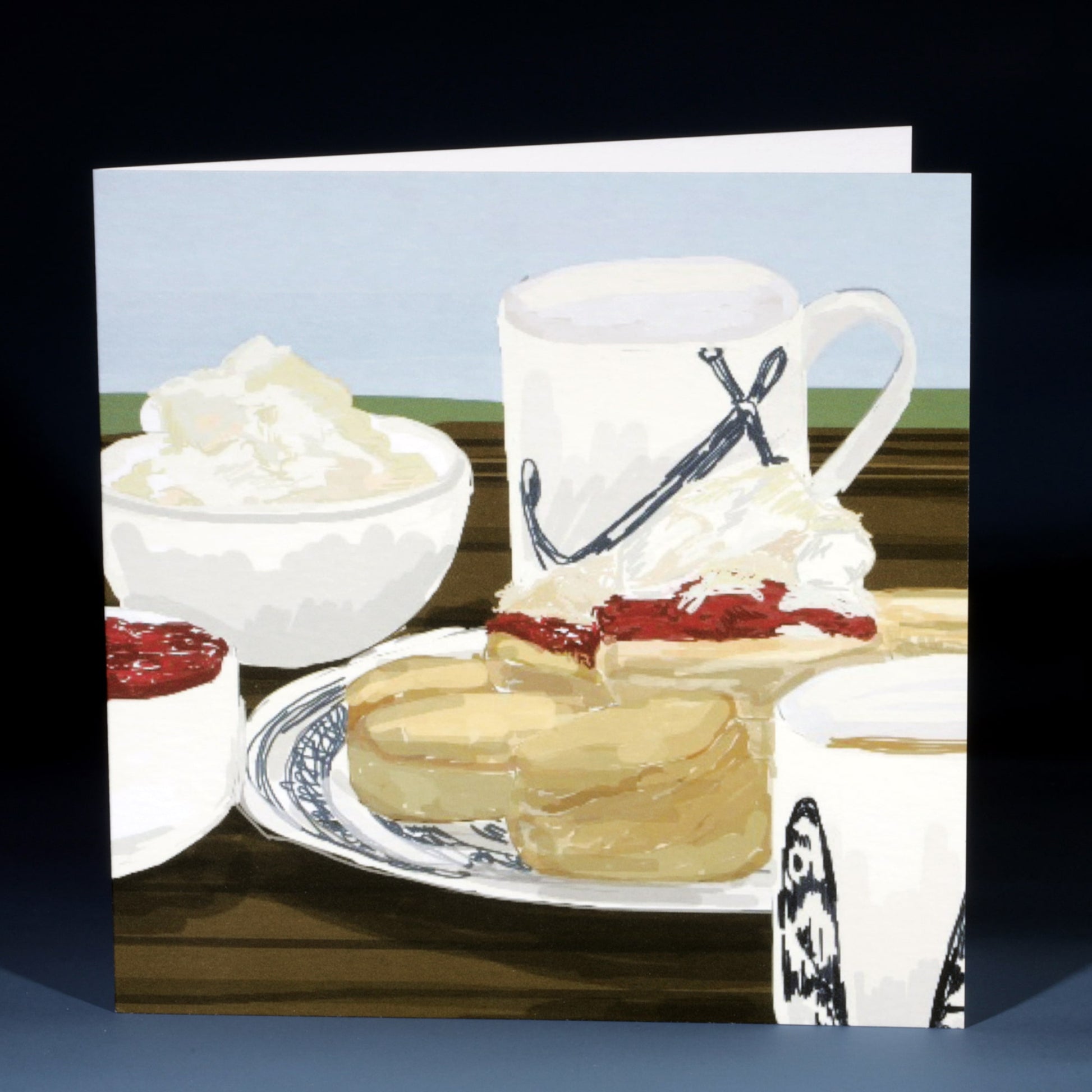 Greeting card featuring an illustrated cream tea scene with scones topped with jam and clotted cream, a bowl of cream, a mug with a nautical rope design, and another patterned mug, all set on a wooden table with a light blue and green background.