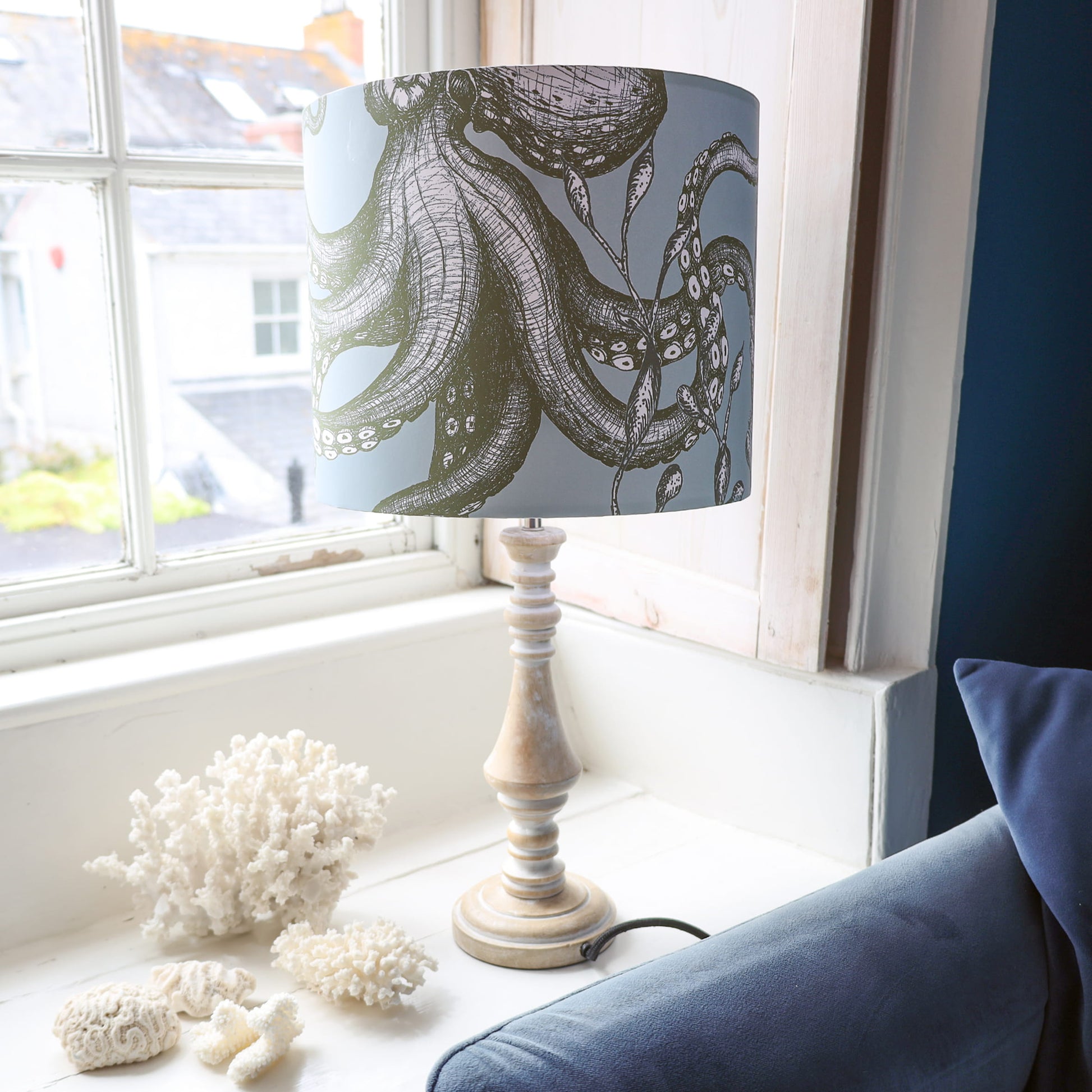 Lamp with an octopus design shade on a windowsill next to decorative corals.