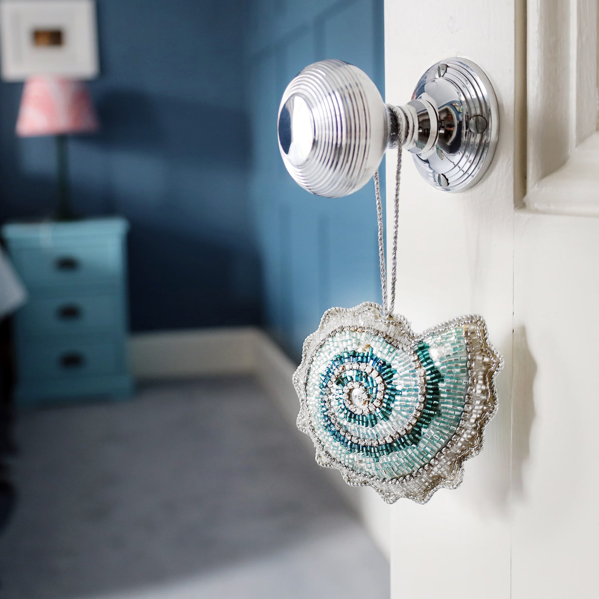 Decorative ammonite-shaped ornament hanging on a silver doorknob with a blurred room background