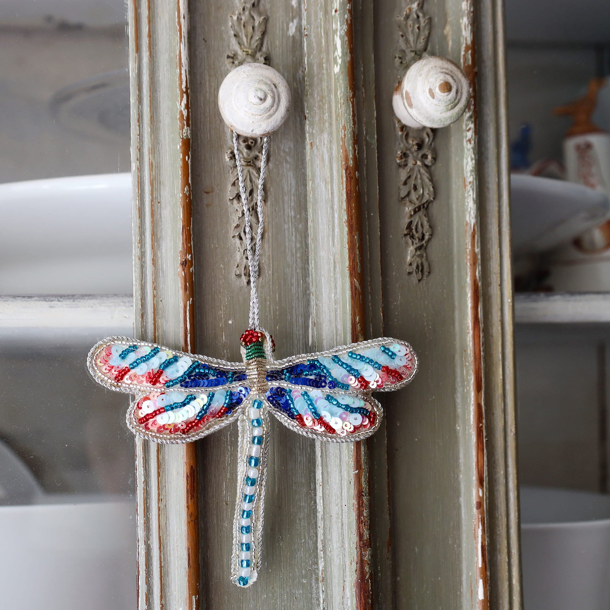 Decorative dragonfly ornament hanging on a textured wall.