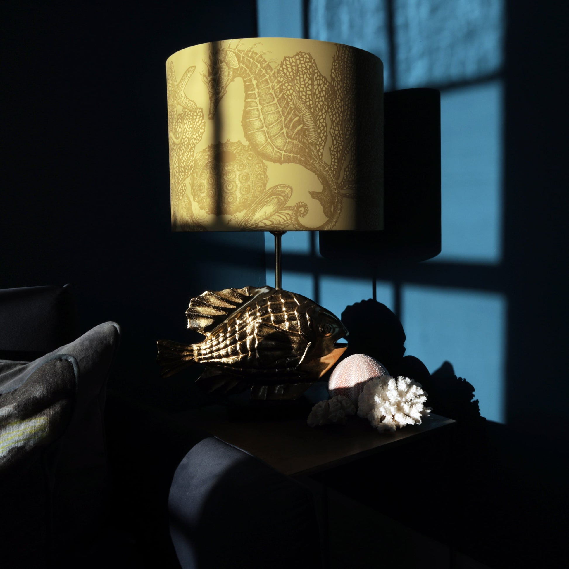 Decorative gold fish lamp base with intricate seahorse design lampshade on a dark background