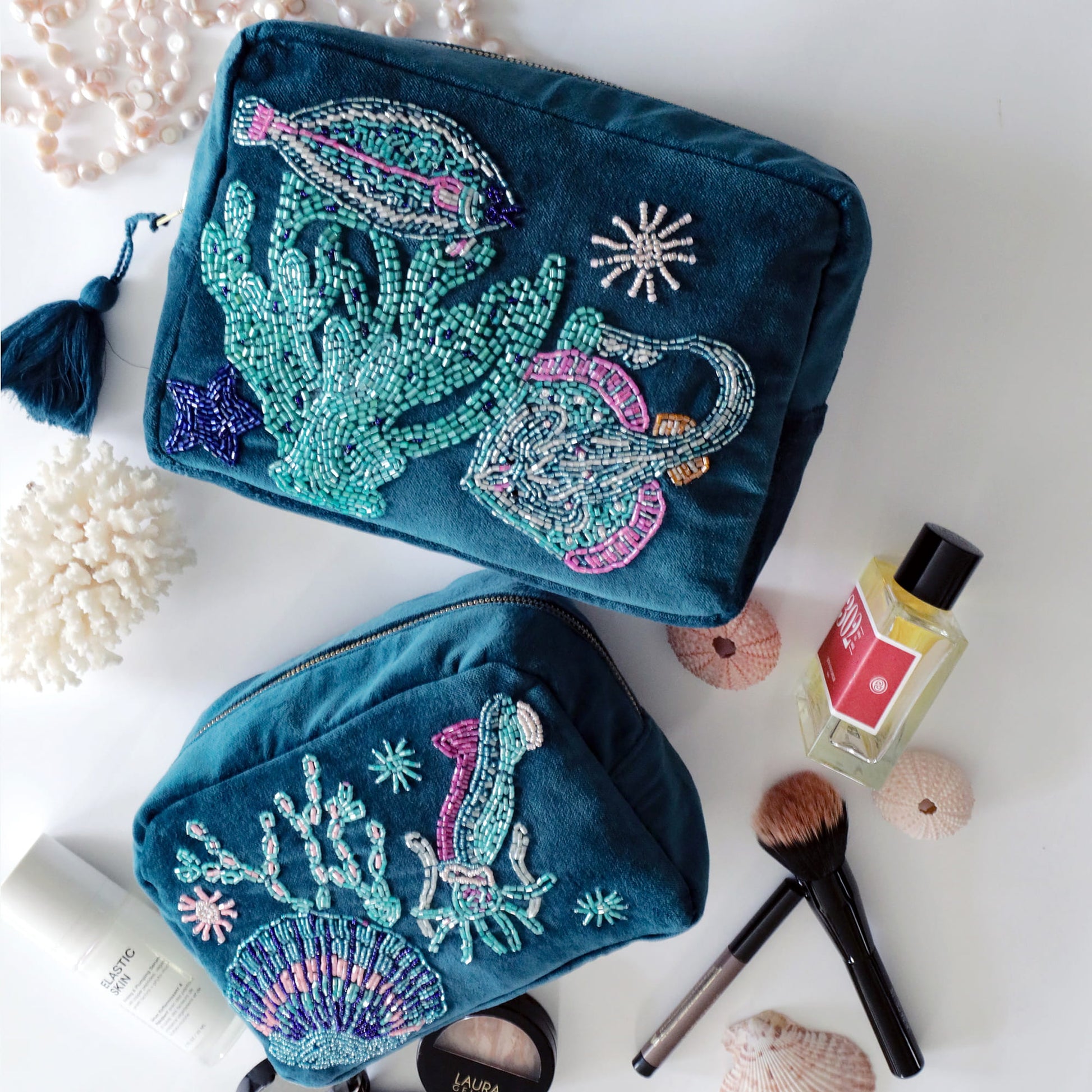 Two teal beaded pouches with sea-themed designs on a white surface with makeup items.